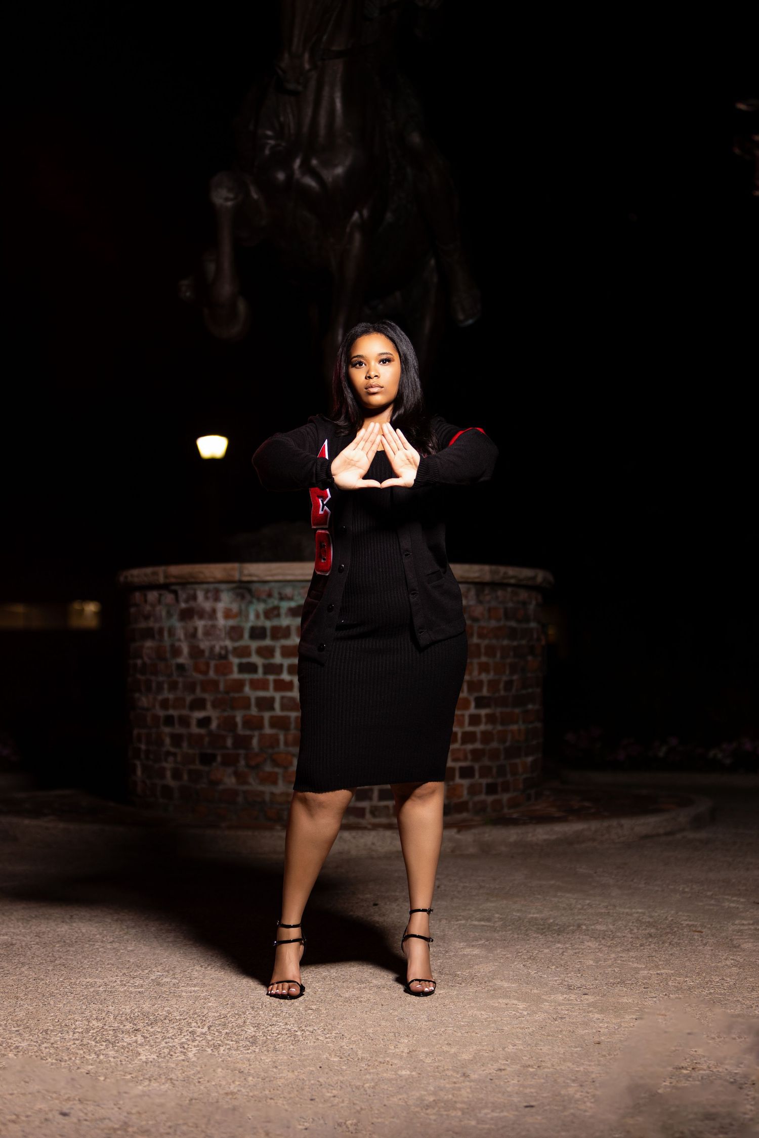 Dramatic nighttime portrait showcasing black dress and heels against brick wall backdrop.