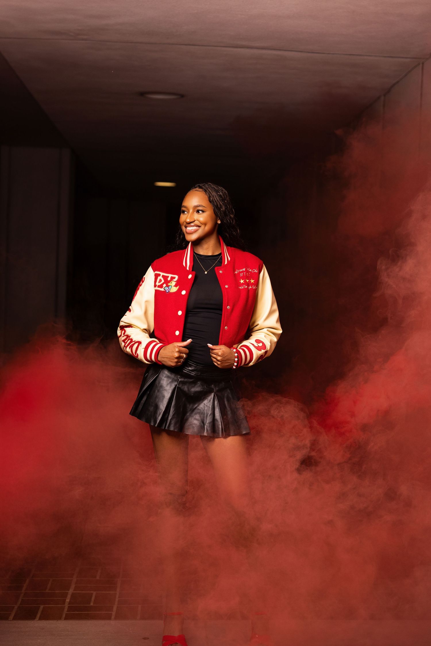 Graduate in varsity jacket poses amid dramatic red smoke effect.
