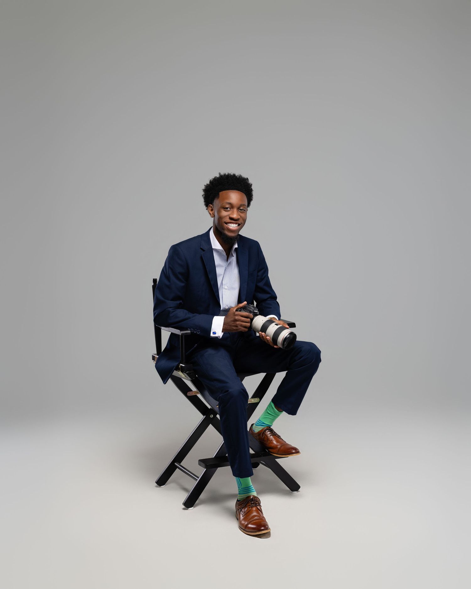 Professional lifestyle portraits showing person in navy suit seated on director's chair against gray studio background.
