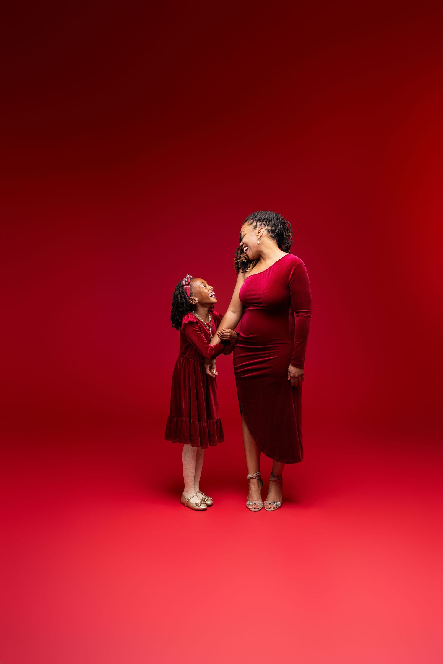 A mother and daughter wearing matching burgundy dresses pose together against a vibrant red background.
