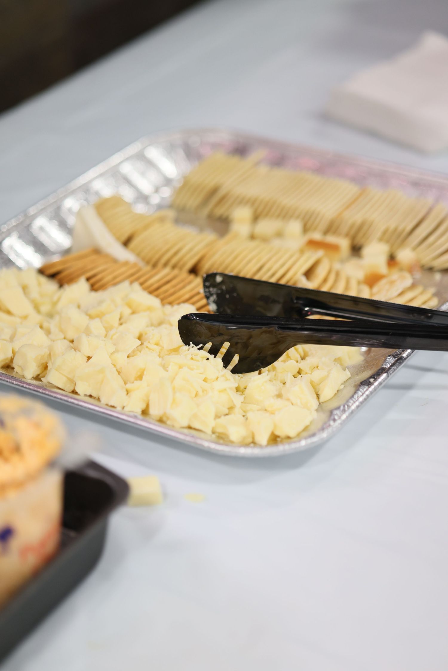 A silver tray with cubed white cheese and crackers, served with black tongs at a catering event.
