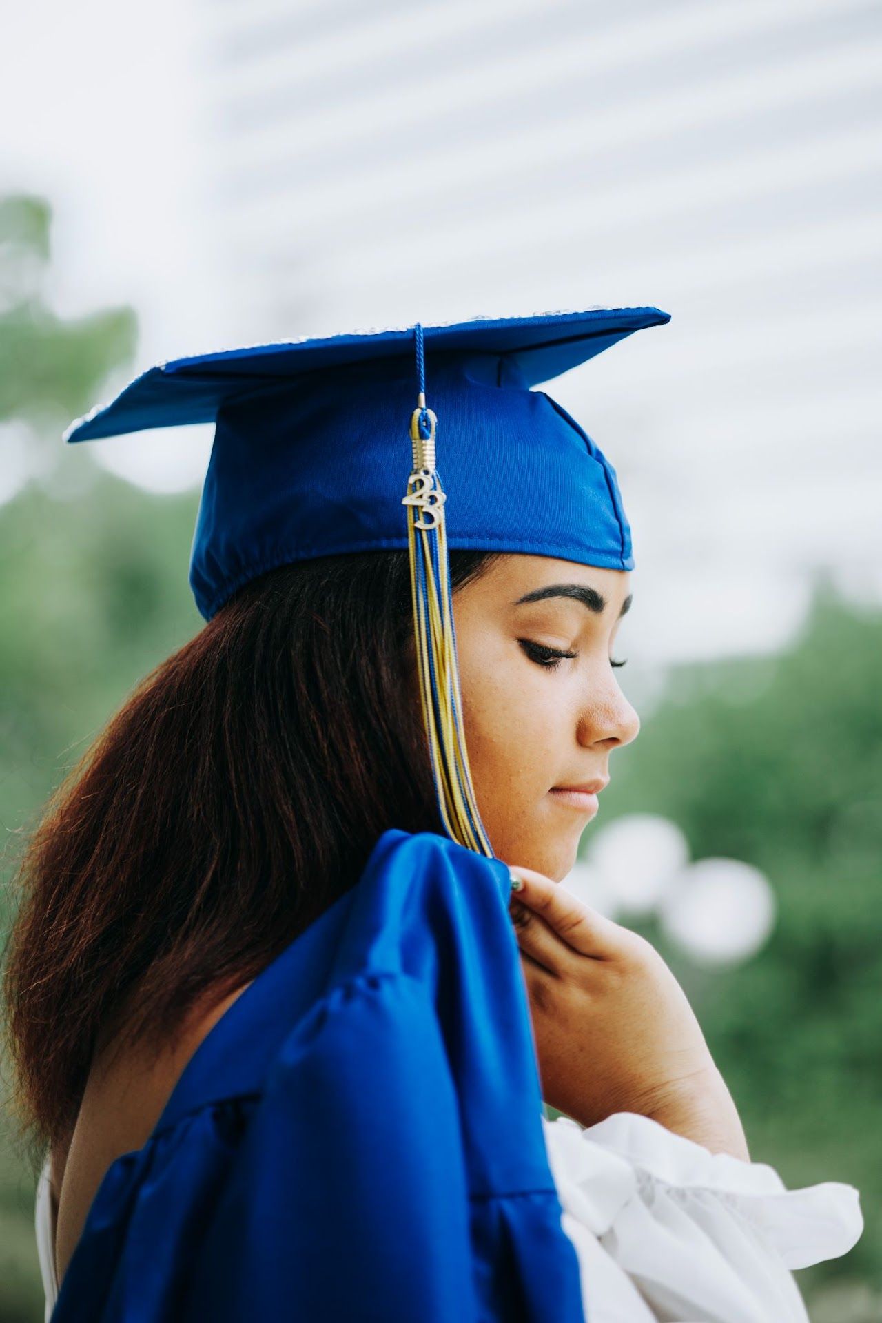 Graduate in blue cap and gown poses for contemplative side profile portrait.