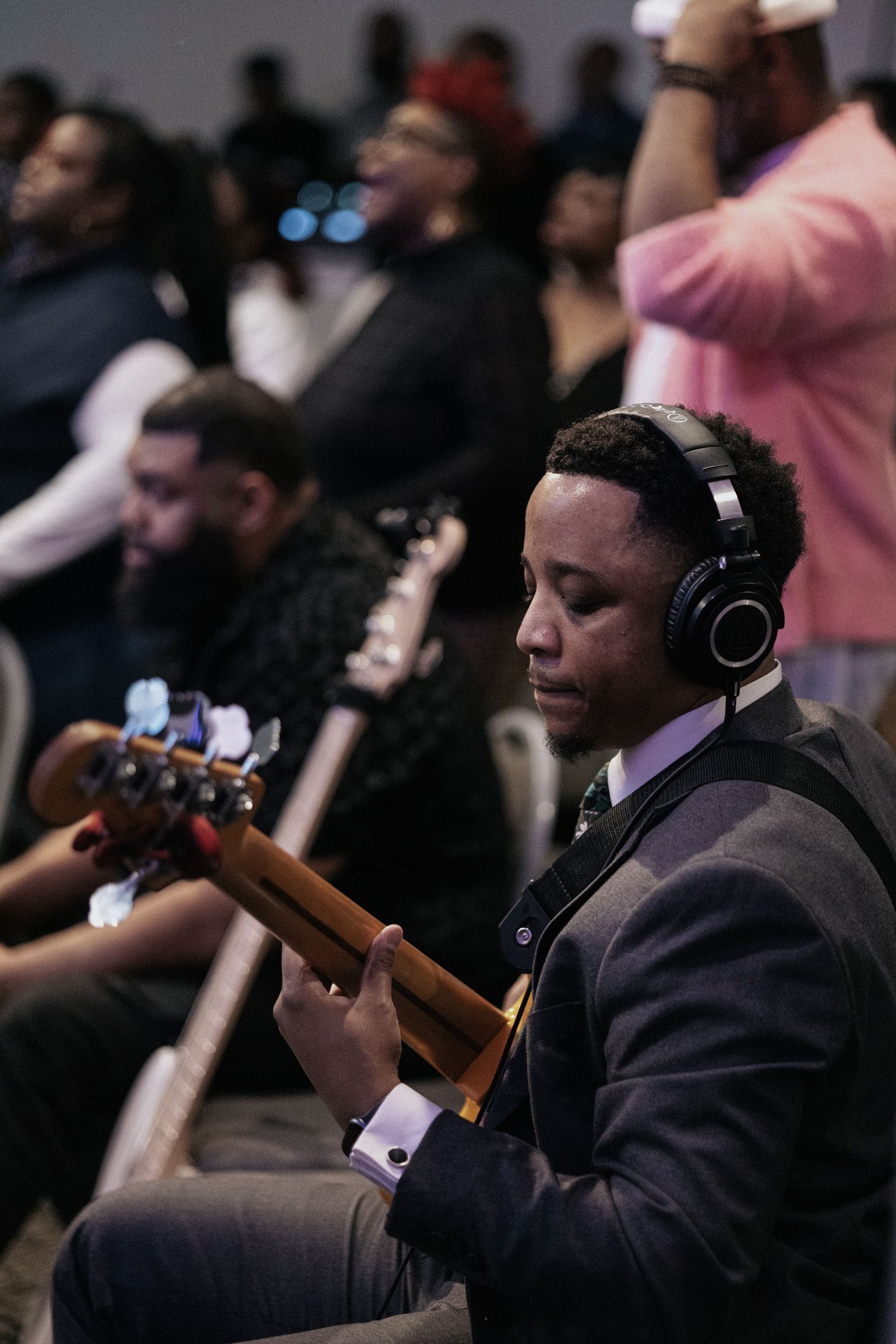 A musician plays bass guitar while wearing headphones during a church performance.