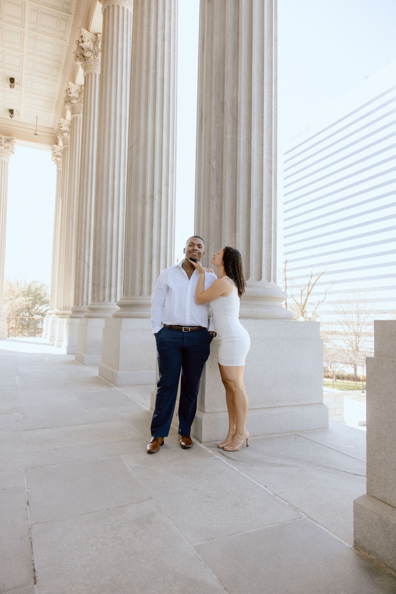 Couple in coordinated white and navy outfits poses between grand marble columns.