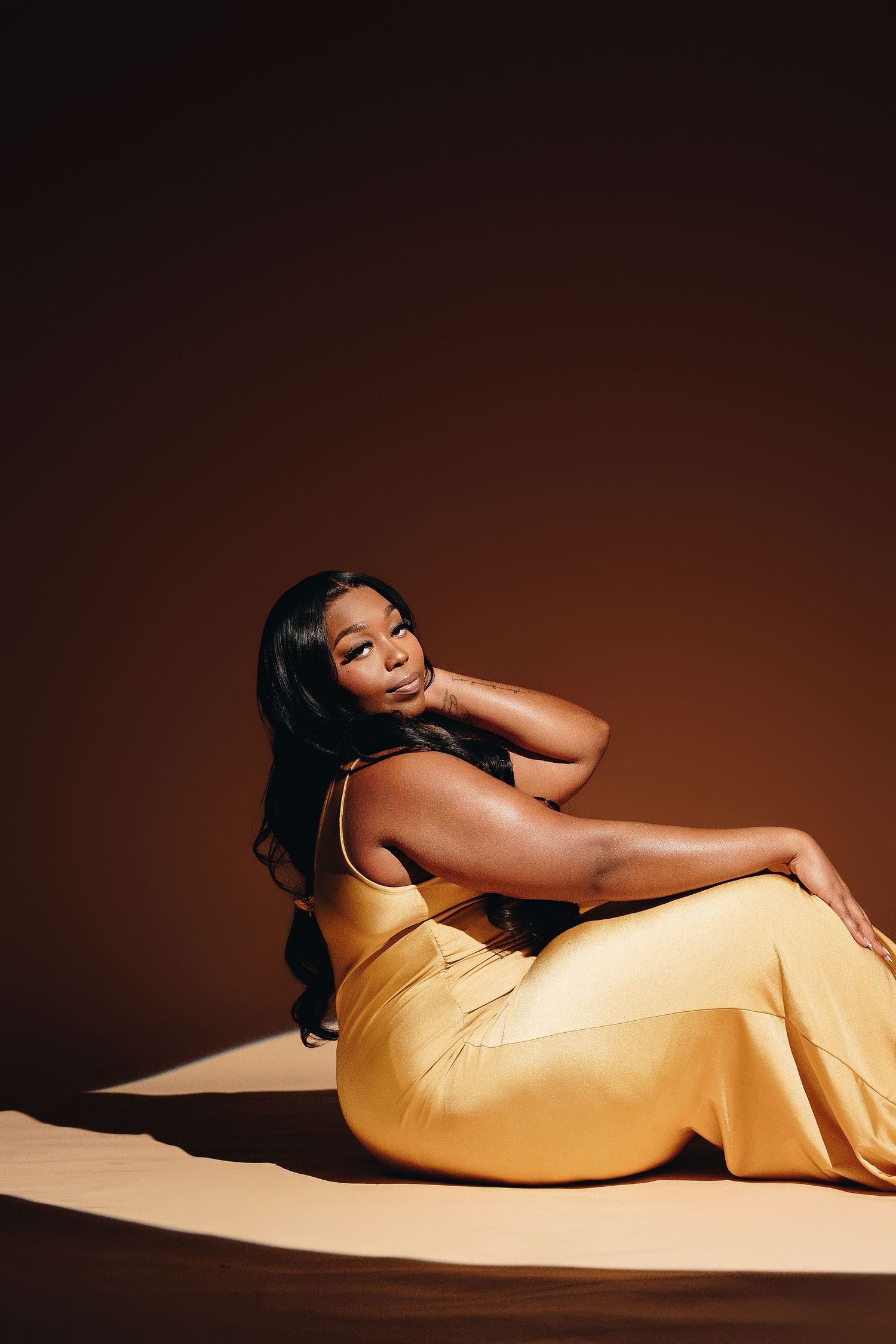 Figure in a sleek yellow dress poses elegantly across a minimalist studio setting with dramatic lighting and shadows.