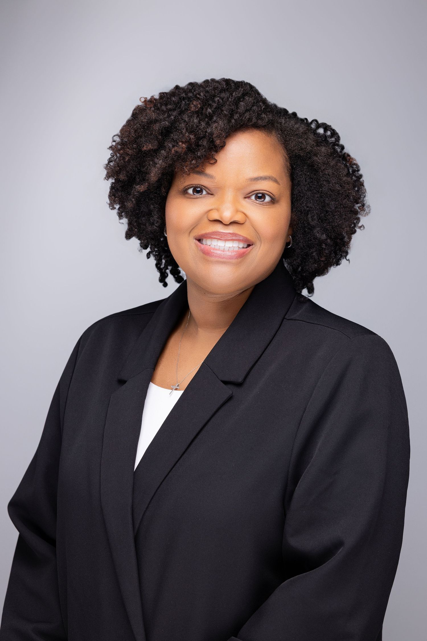 Professional studio portrait series showing a person in a black blazer and white top against a gray background with natural curly hair.