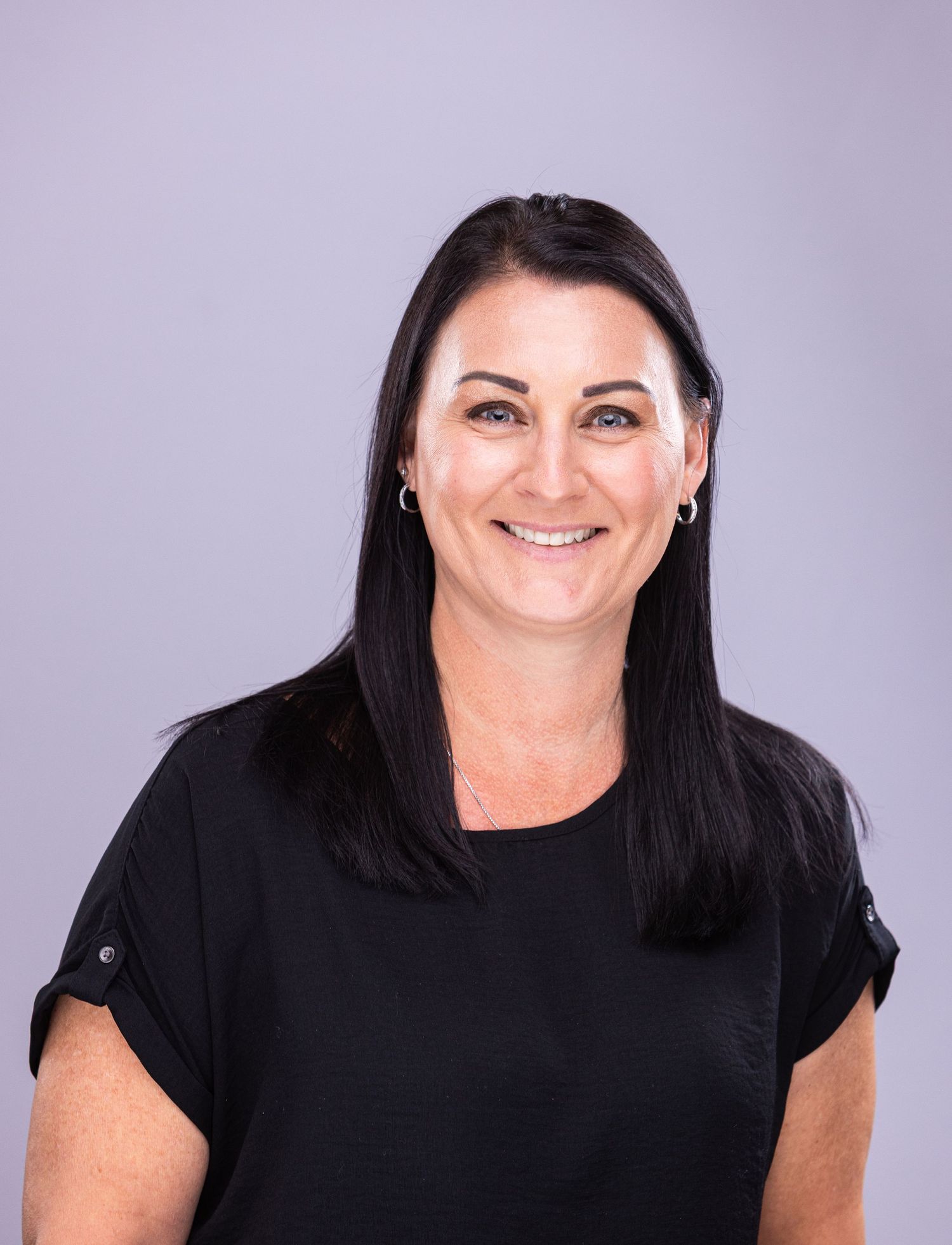 Professional headshot of person with dark hair wearing black top against purple background.