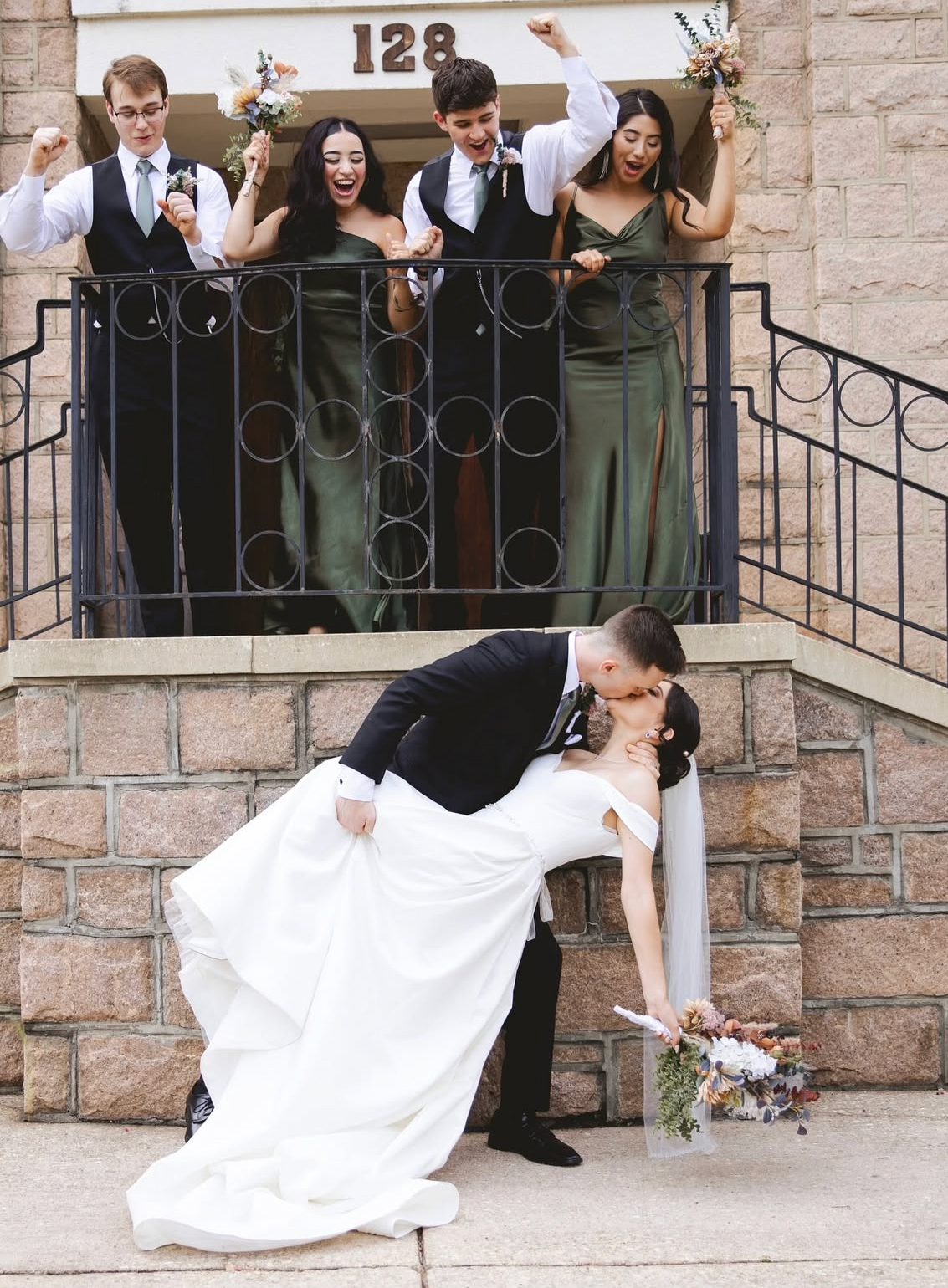 Wedding party members lean over a stone railing while bride and groom share a romantic dip pose below.