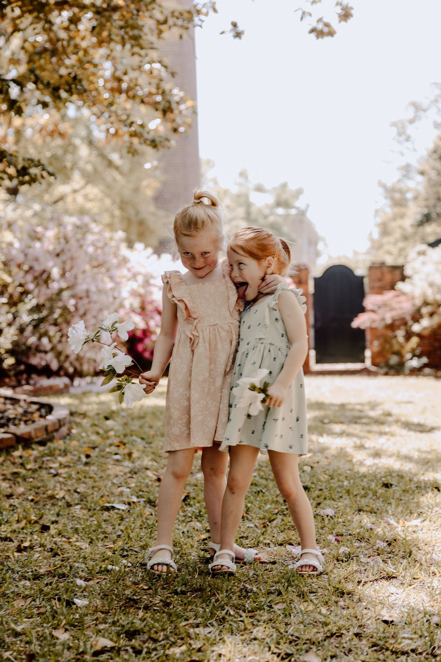 Two young children in vintage clothing giggle together while playing in a sunlit garden.