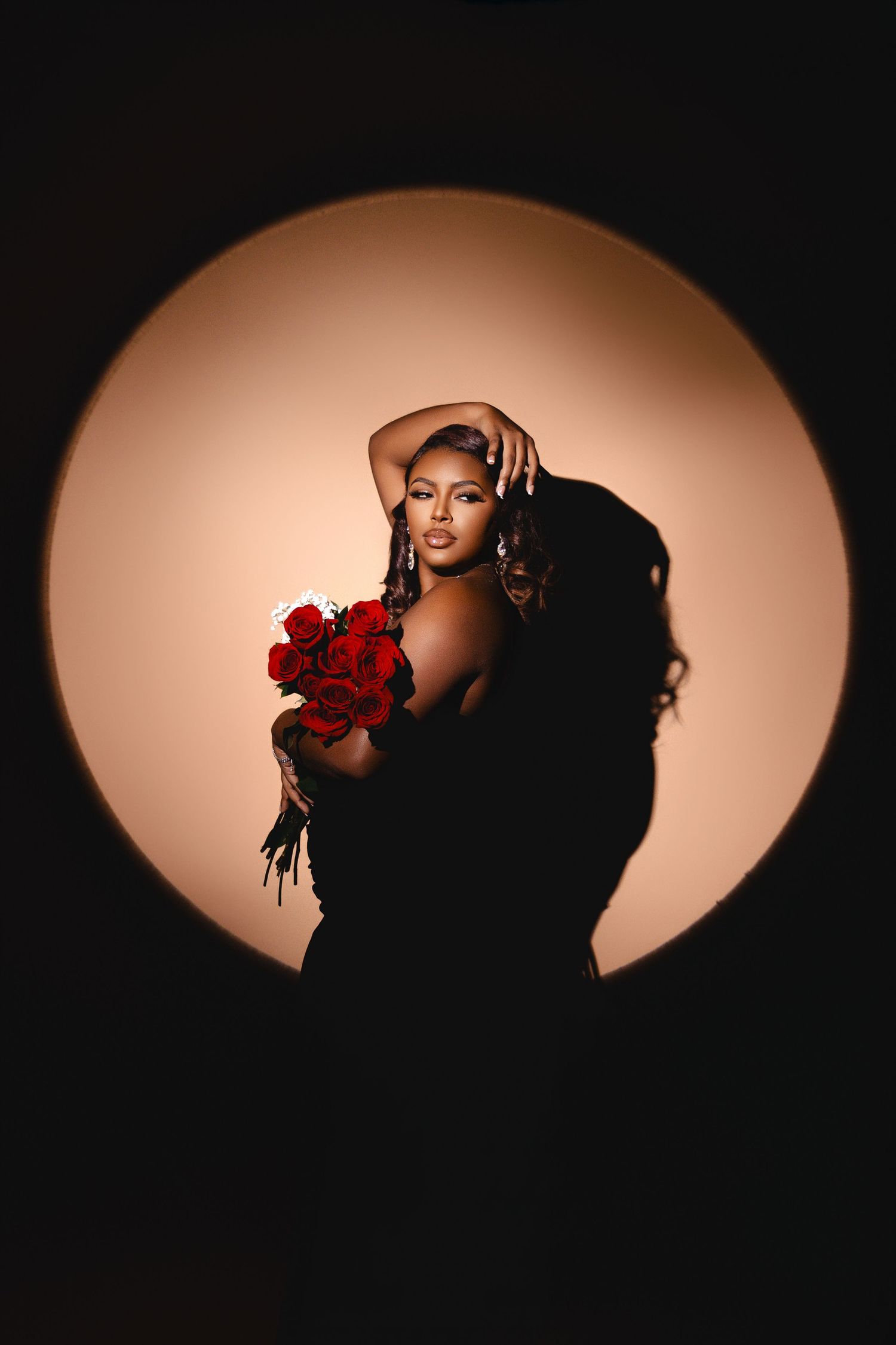 Artistic silhouette photo with model holding red roses against circular warm backdrop.