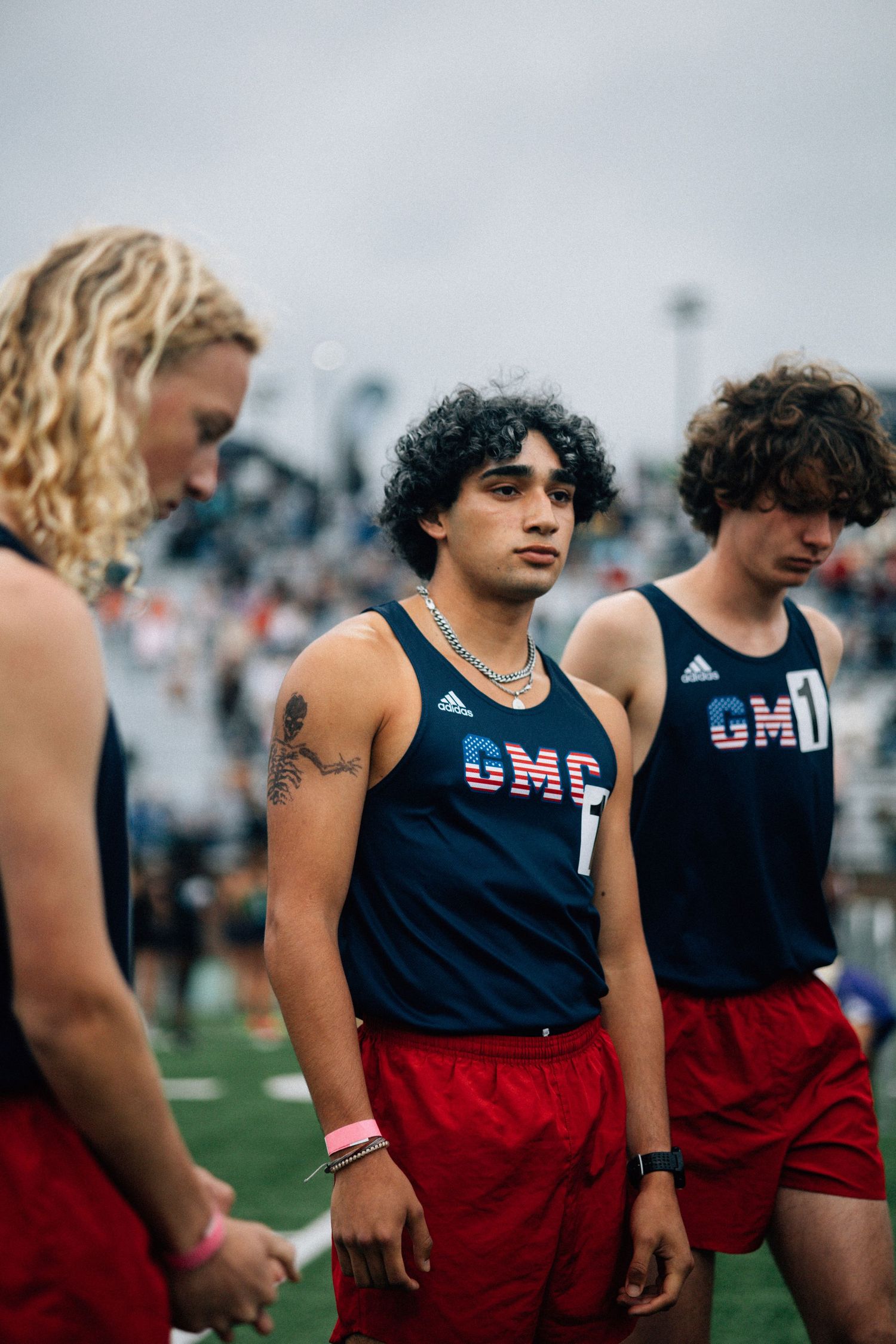 Track athletes in navy CMP uniforms stand together on field during competition.