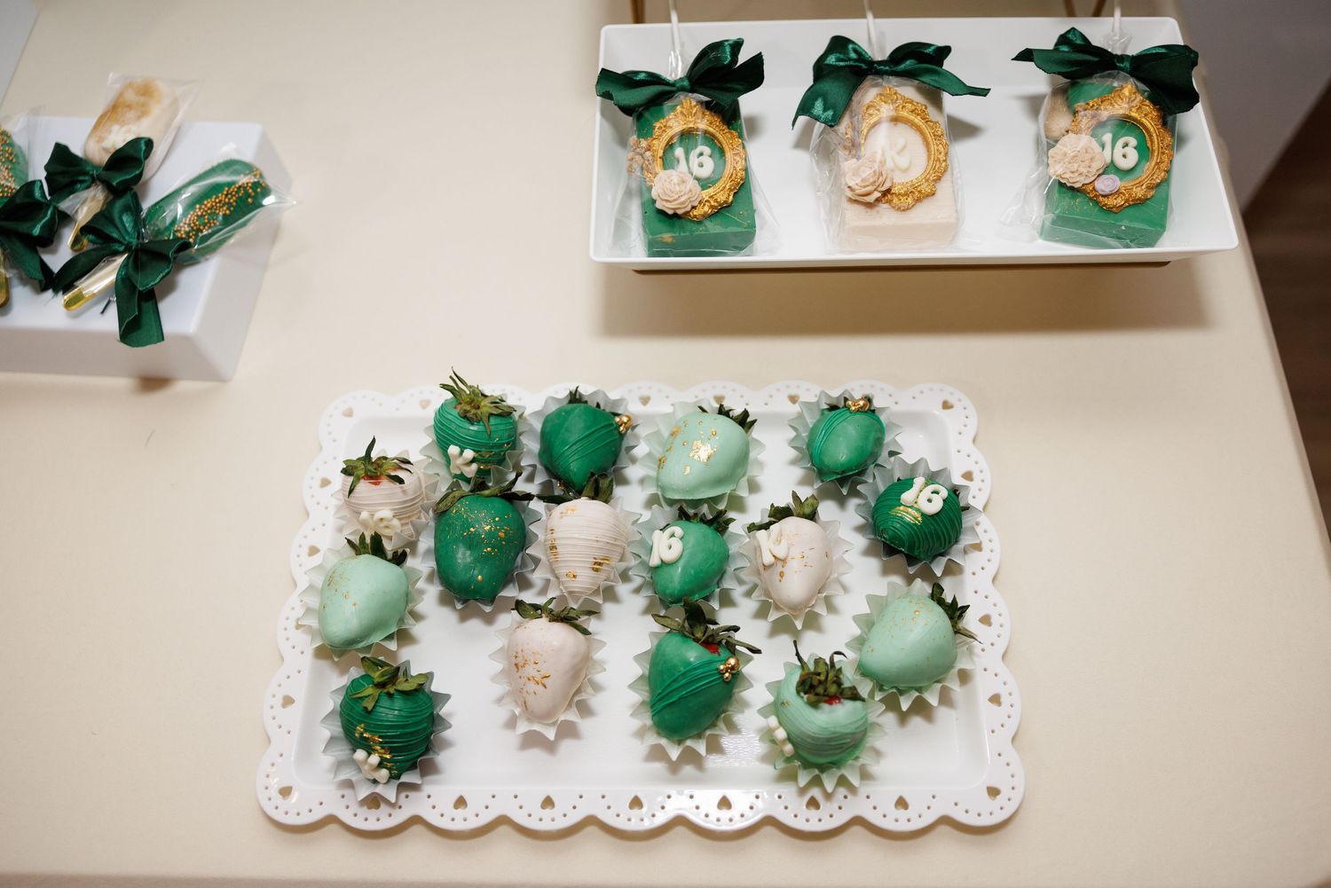 Green and white chocolate-covered strawberries with gold accents on a decorative tray, with gift boxes tied with green ribbons.