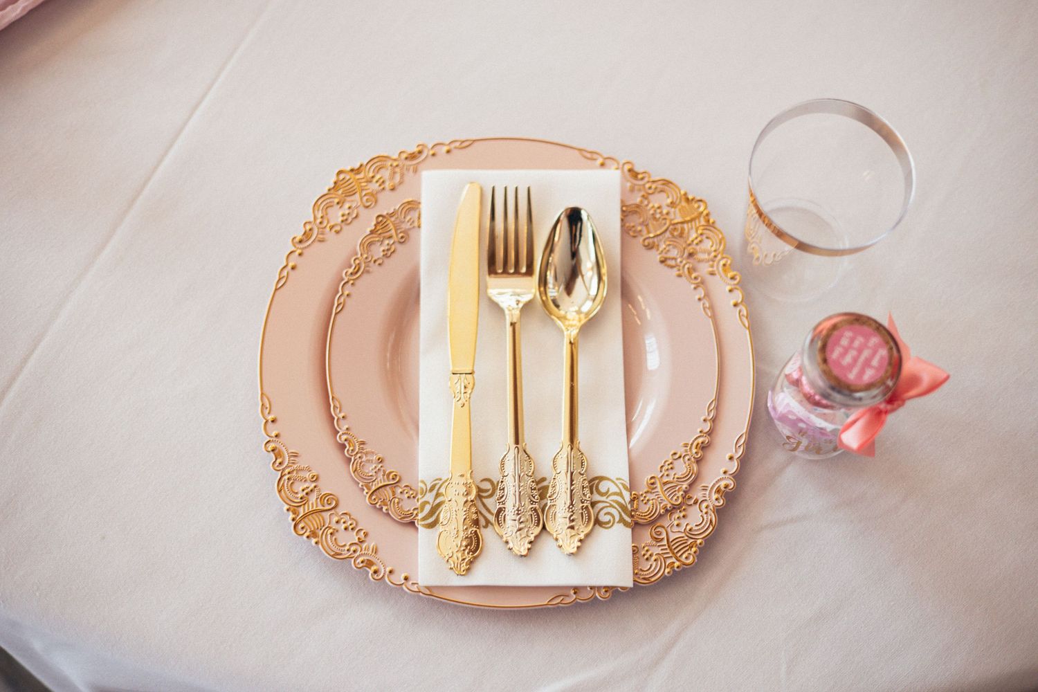 Elegant gold flatware set on white napkin atop ornate pink charger plate for formal table setting.