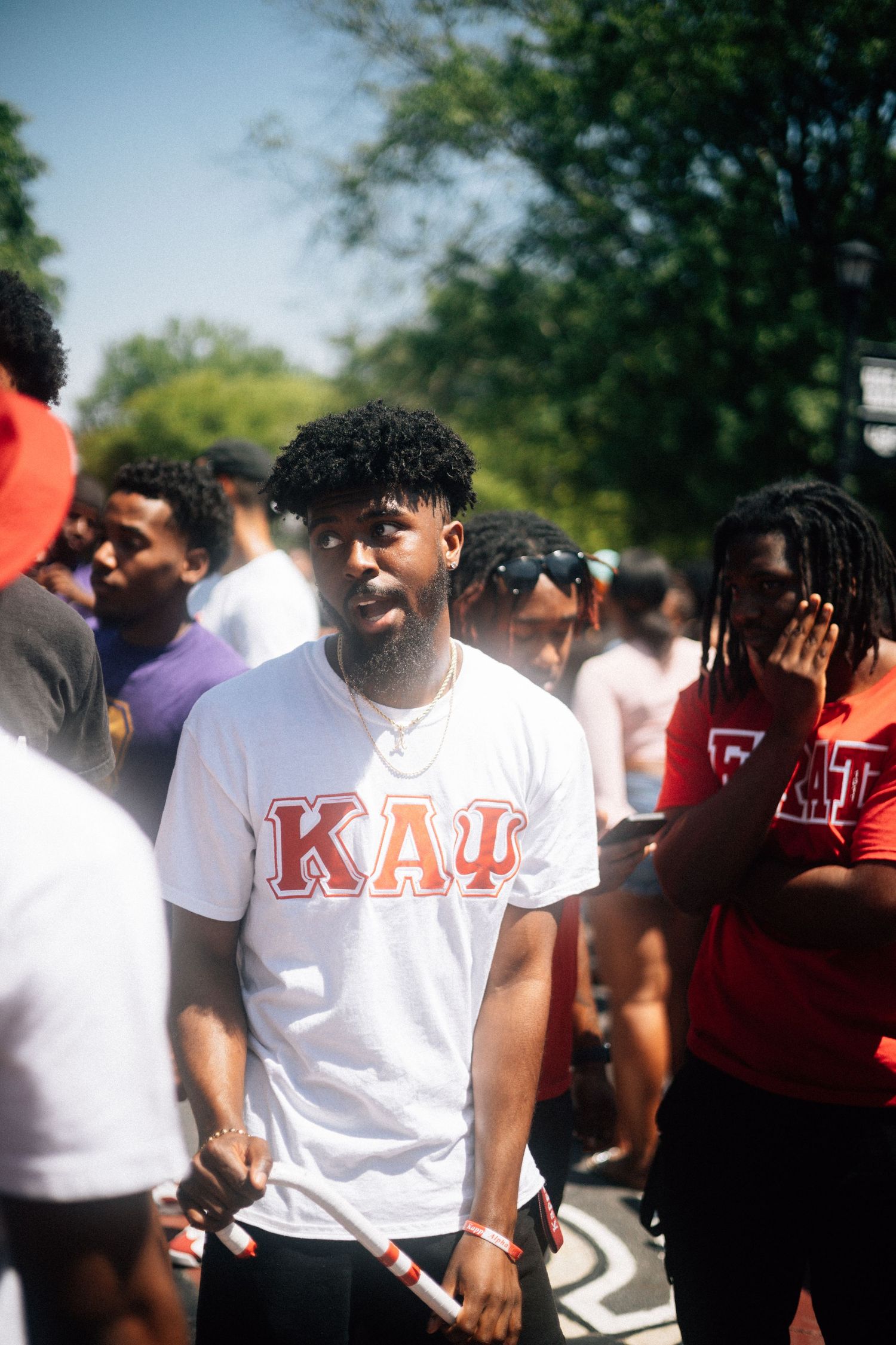 Group of students gathered outdoors on a sunny day, with one wearing a white t-shirt with Greek letters.  USC Hip Hop Wednesday