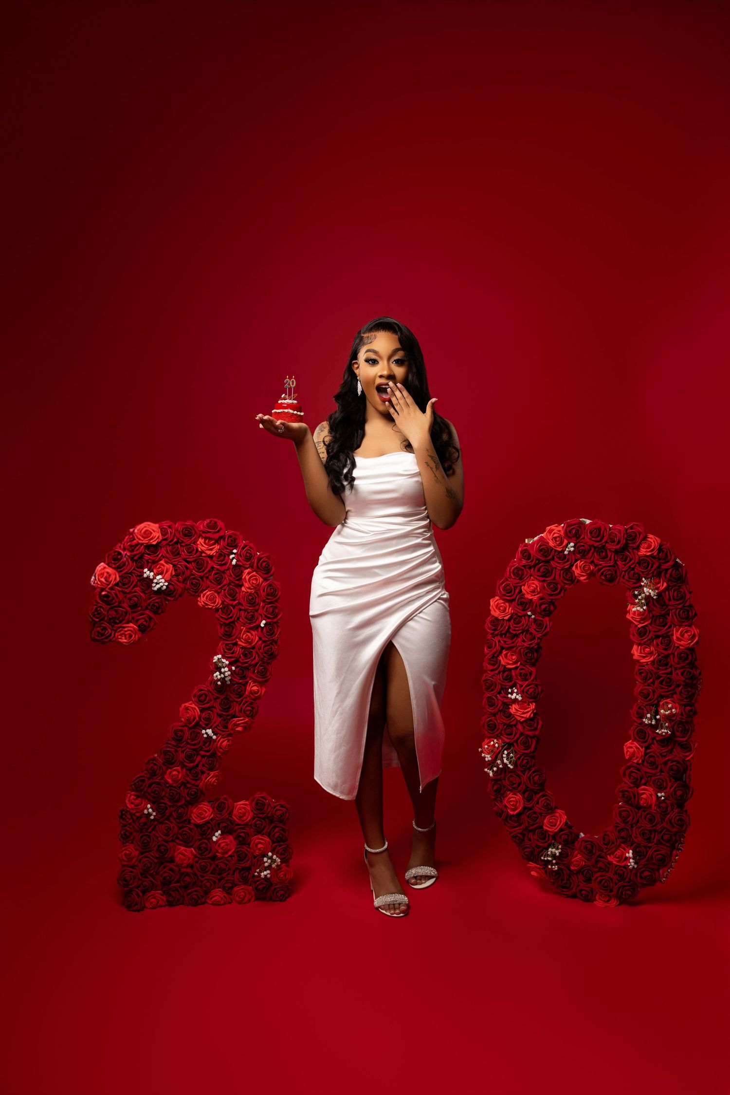 Elegant photo setup with floral 2020 numbers and white dress against deep red background.