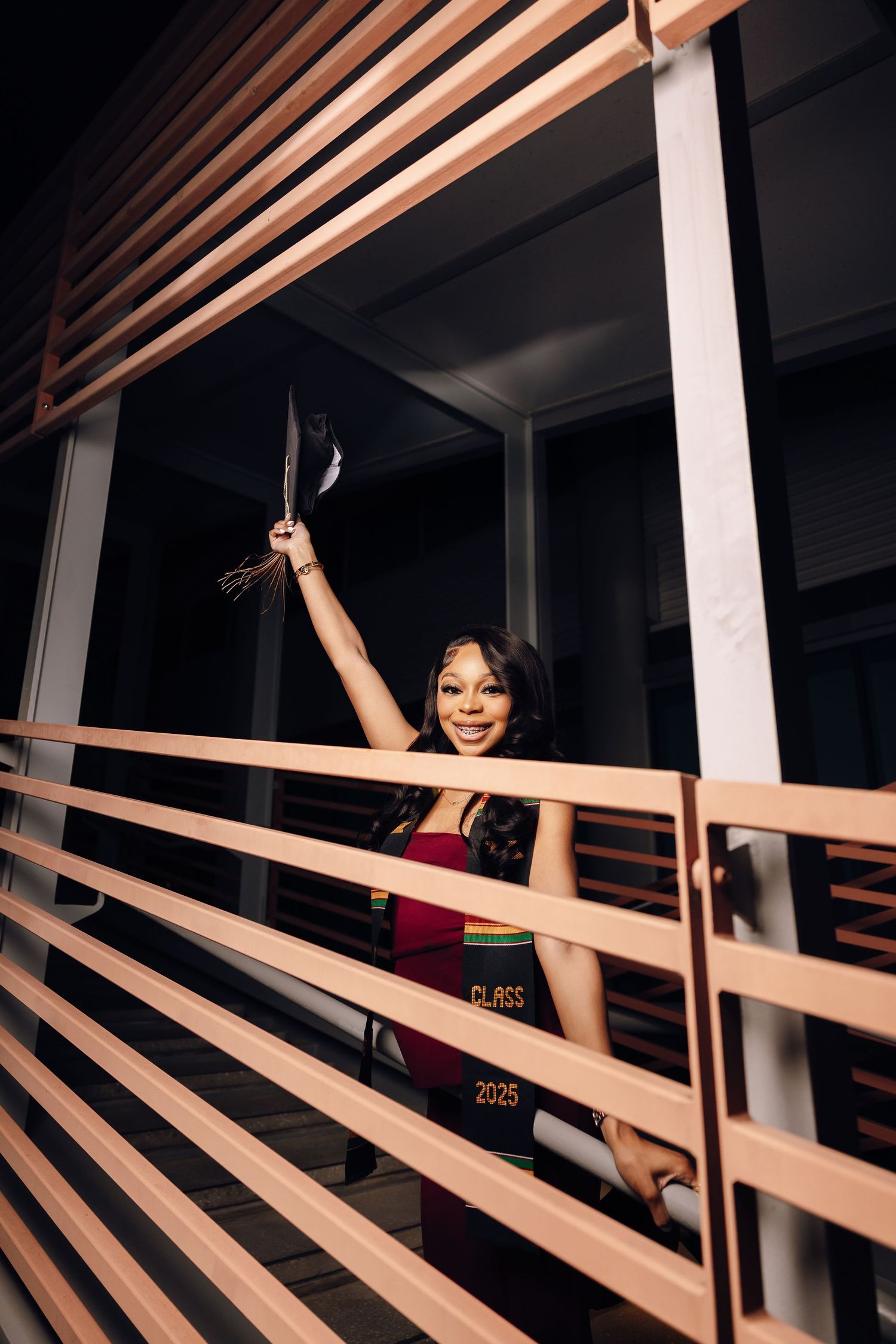 Graduate poses through wooden slats in modern architectural setting.