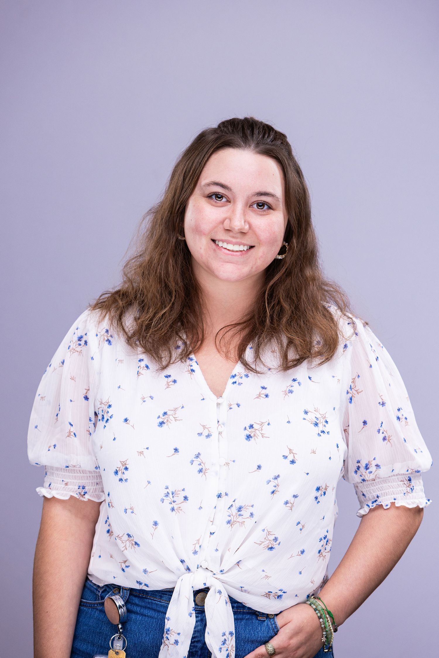Professional portrait of person in floral tie-front blouse against purple background.