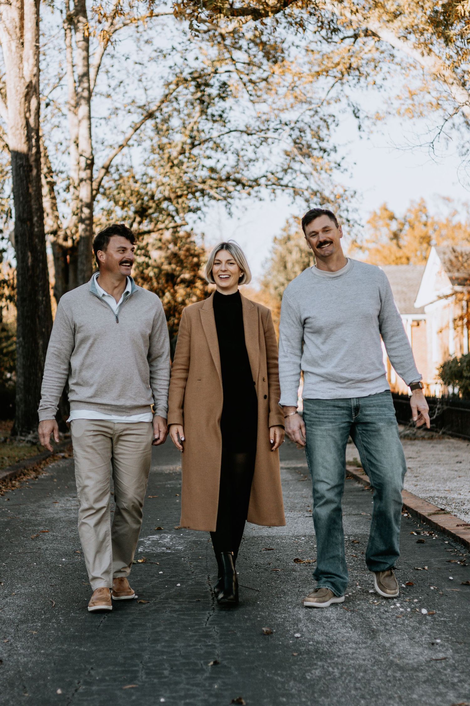 Three people walking together on a tree-lined path during autumn.