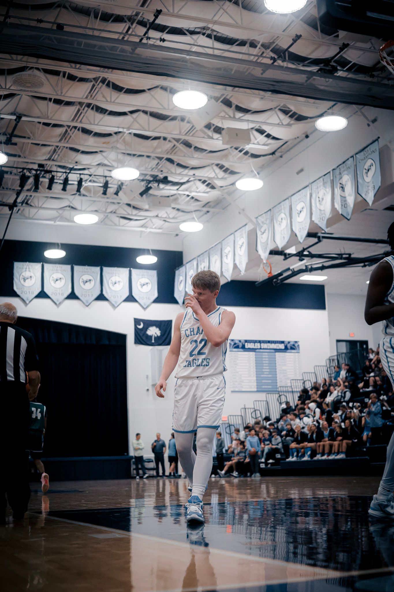 Basketball player shooting in white uniform under championship banners in gymnasium.