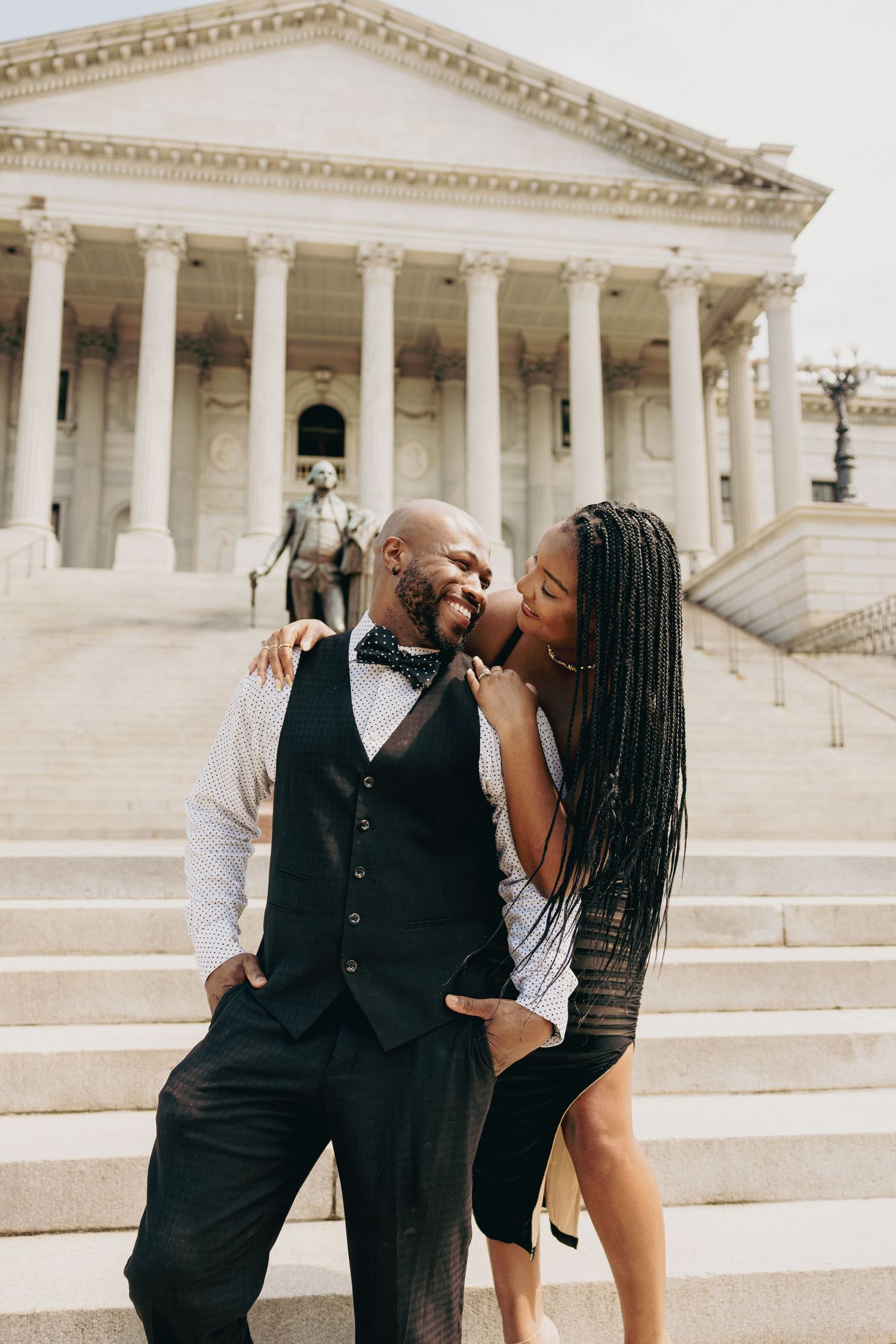 Couple embracing on steps of historic building with white columns.