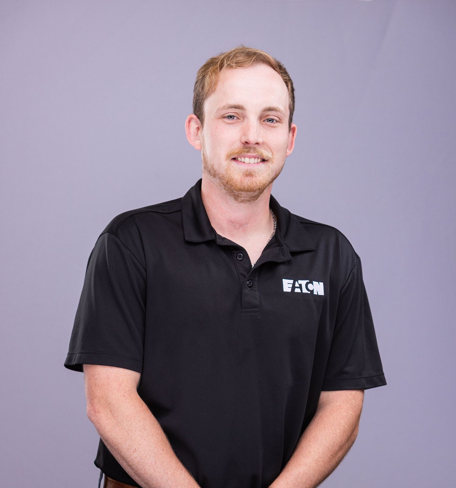 Professional portrait of person in black Eaton polo shirt against purple background.