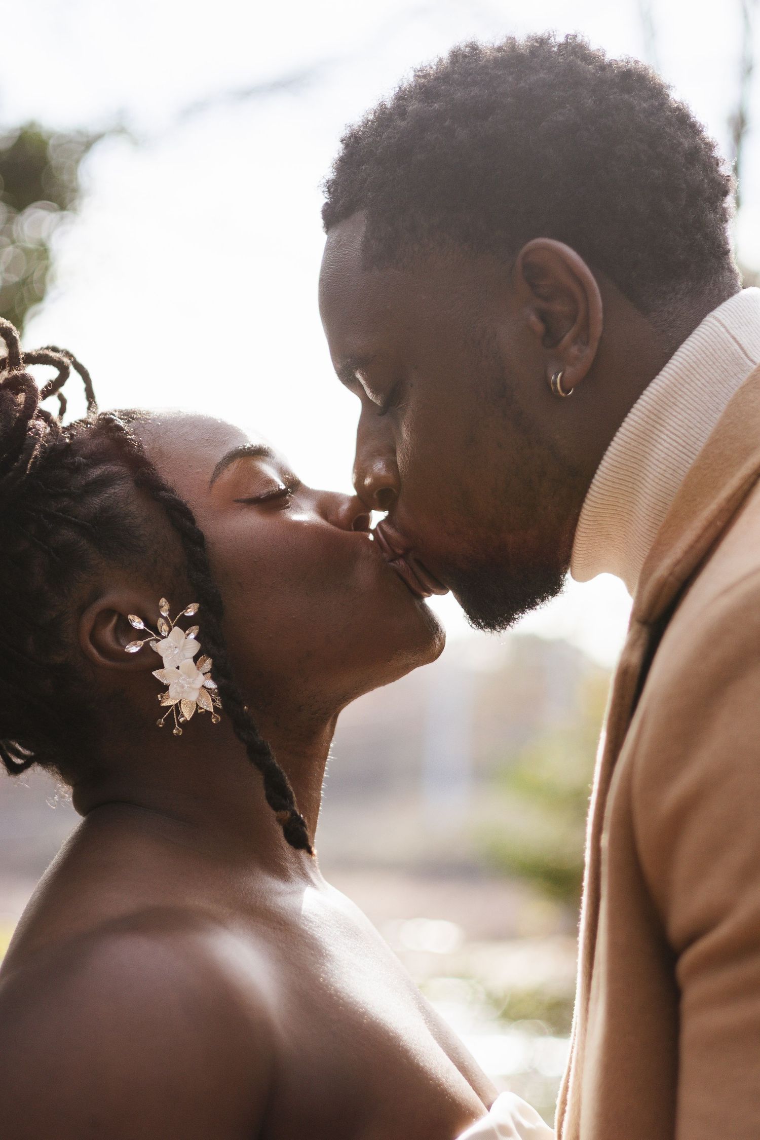 Tender moment between couple in formal wedding attire against sunlit background.