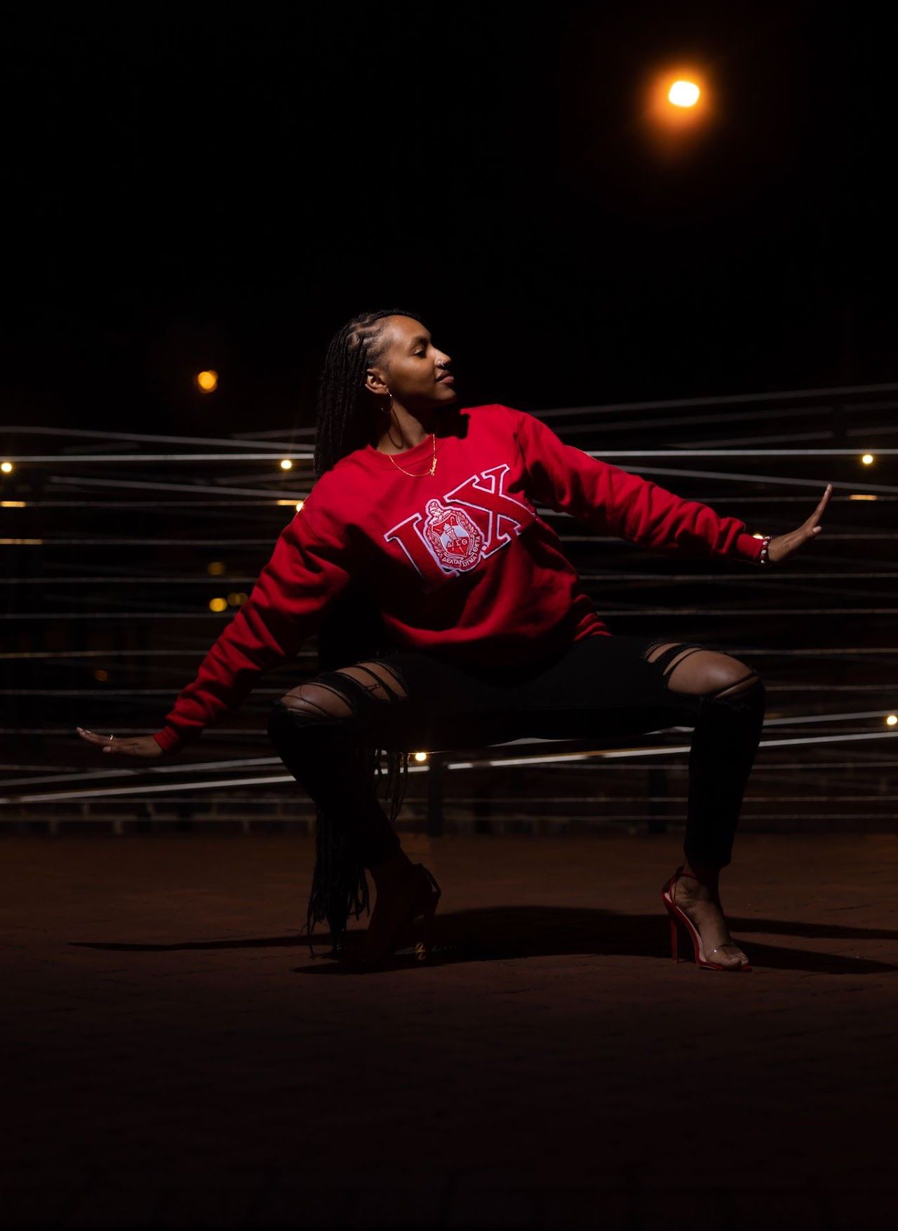 A dancer in a red sweatshirt and dark pants strikes a graceful pose at night under street lights.