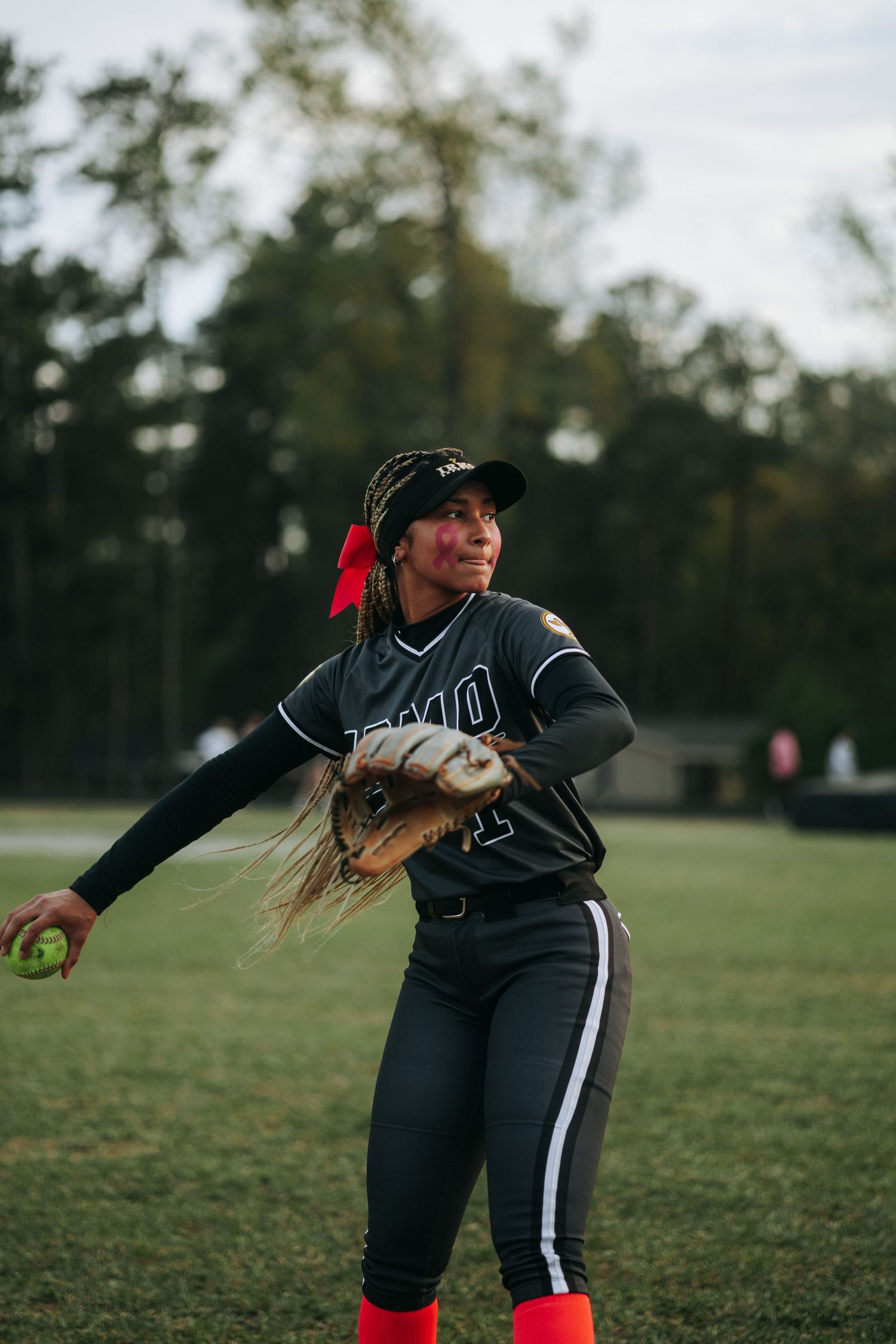 Irmo HS Softball player in a dark uniform and red socks winds up for a pitch on a grassy field at dusk.