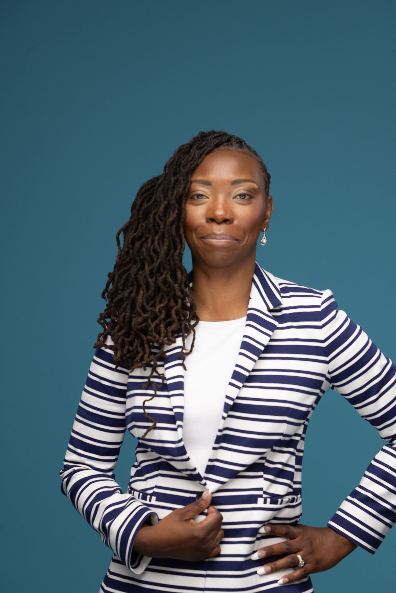 Professional headshot of person in striped blazer against teal background.