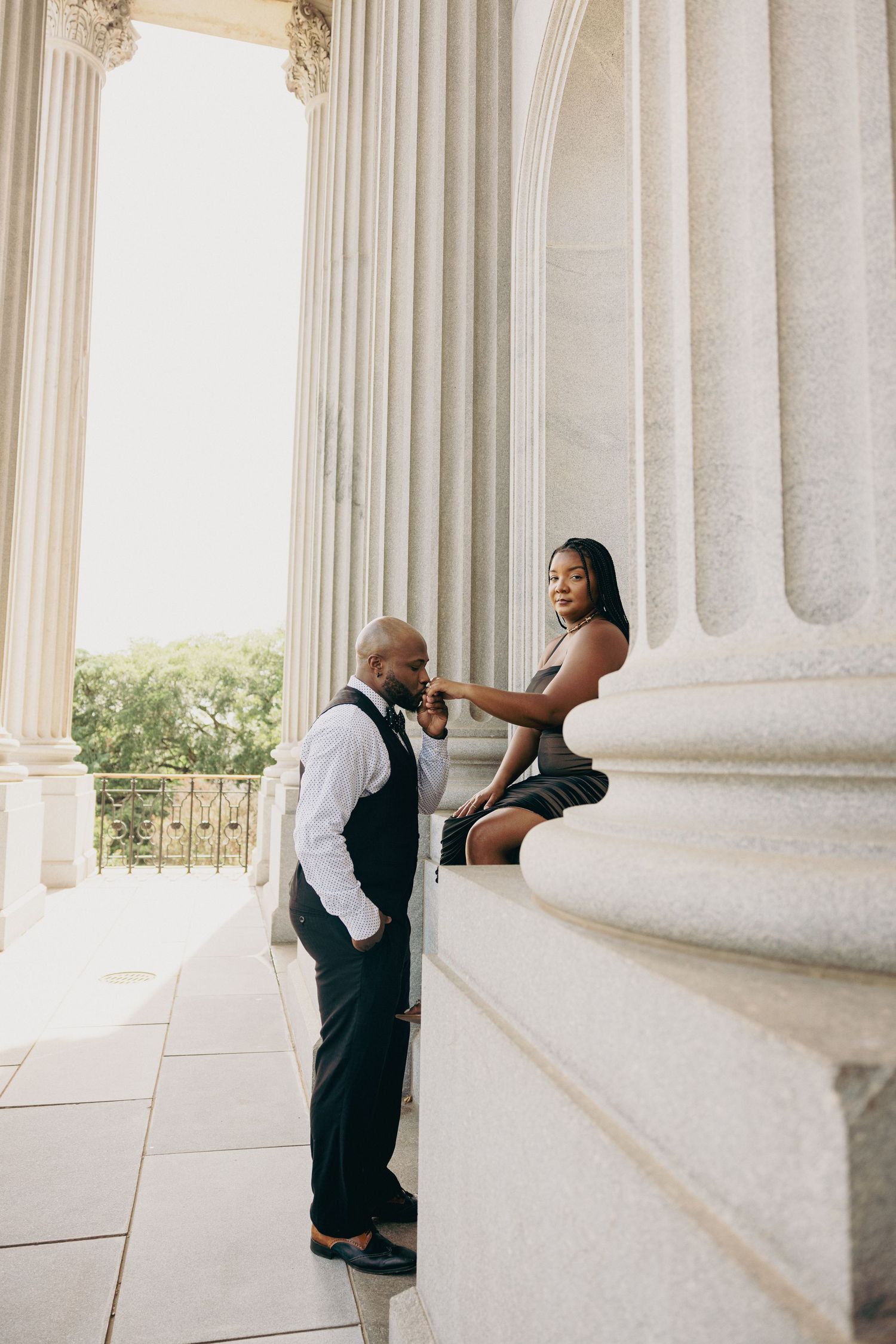 Couple posing playfully between classical columns in formal wear.
