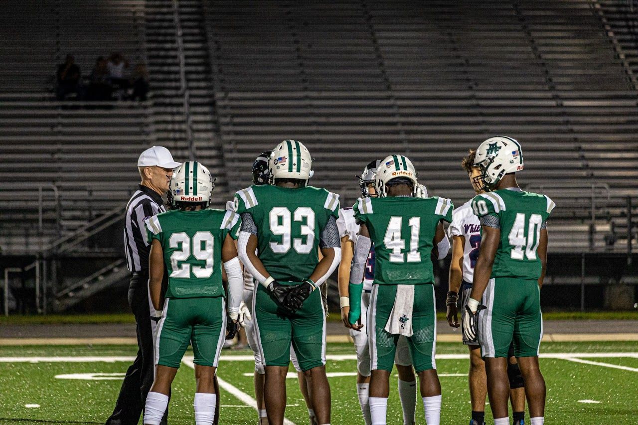 Football players in green jerseys line up on field during practice or game preparation. DFHS