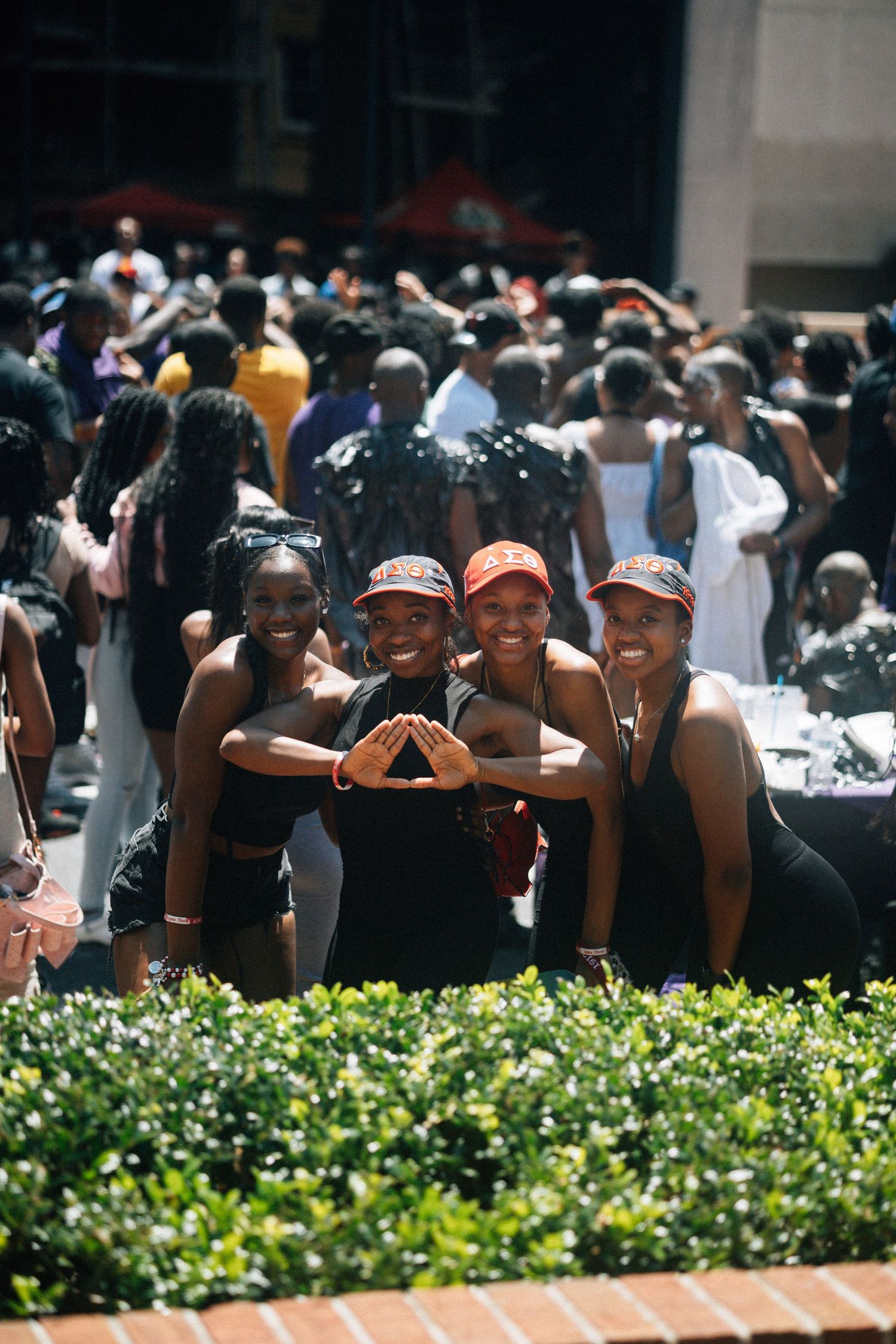 A group of friends pose together wearing matching black outfits at an outdoor event with a crowd behind them.  USC Hip Hop Wednesday