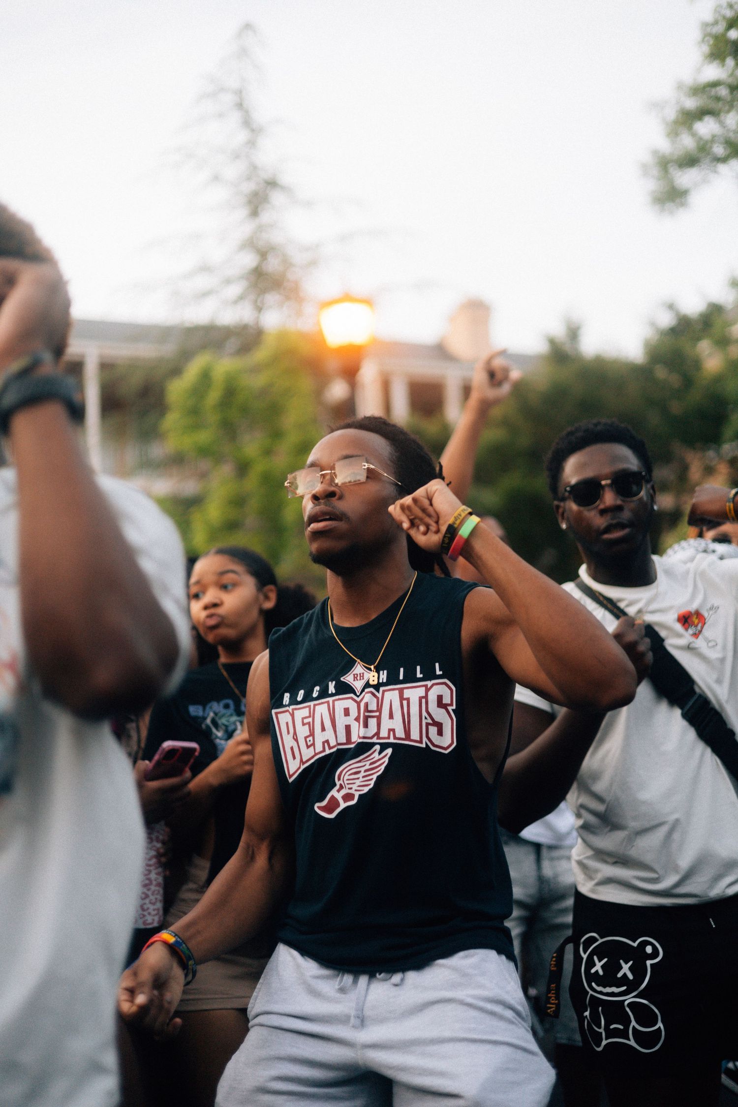 Group of students in a Cincinnati Bearcats shirt celebrating outdoors at sunset with raised arms and energetic moves. USC Hip Hop Wednesday