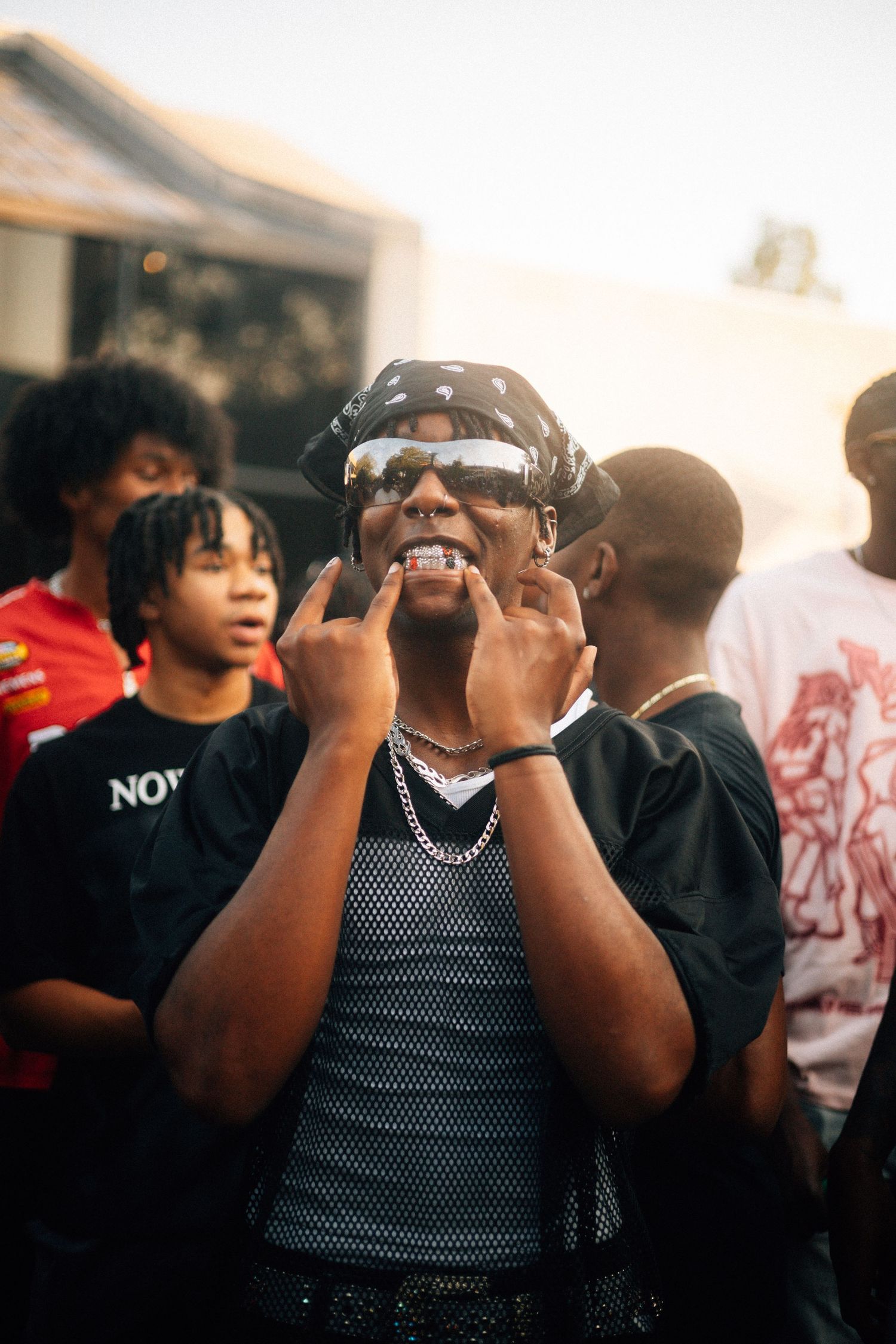 A person in sunglasses and mesh tank top shows excitement while standing in a crowd at an outdoor event.