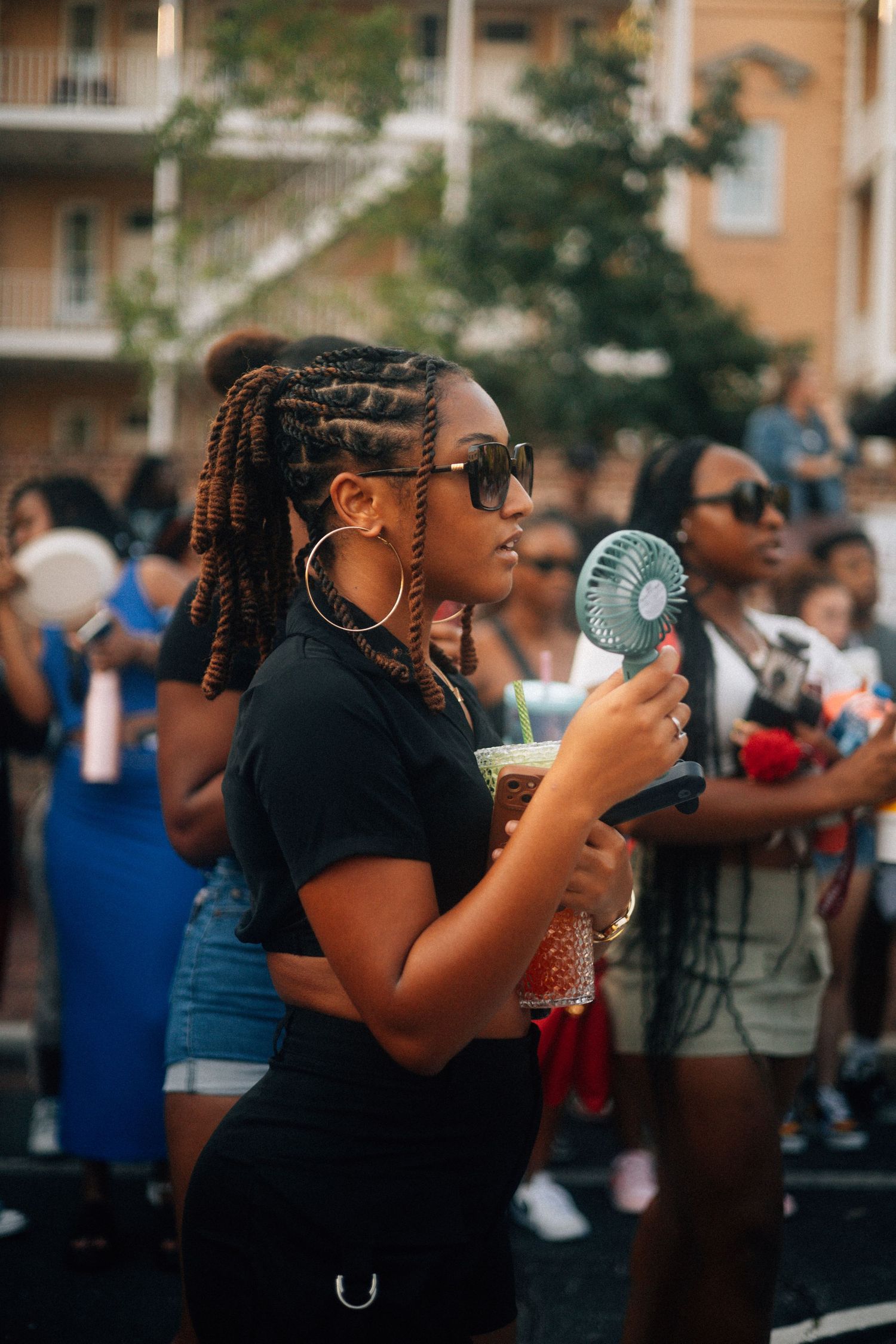 Someone with braided hair and sunglasses holds a portable fan at an outdoor summer event.  USC Hip Hop Wednesday