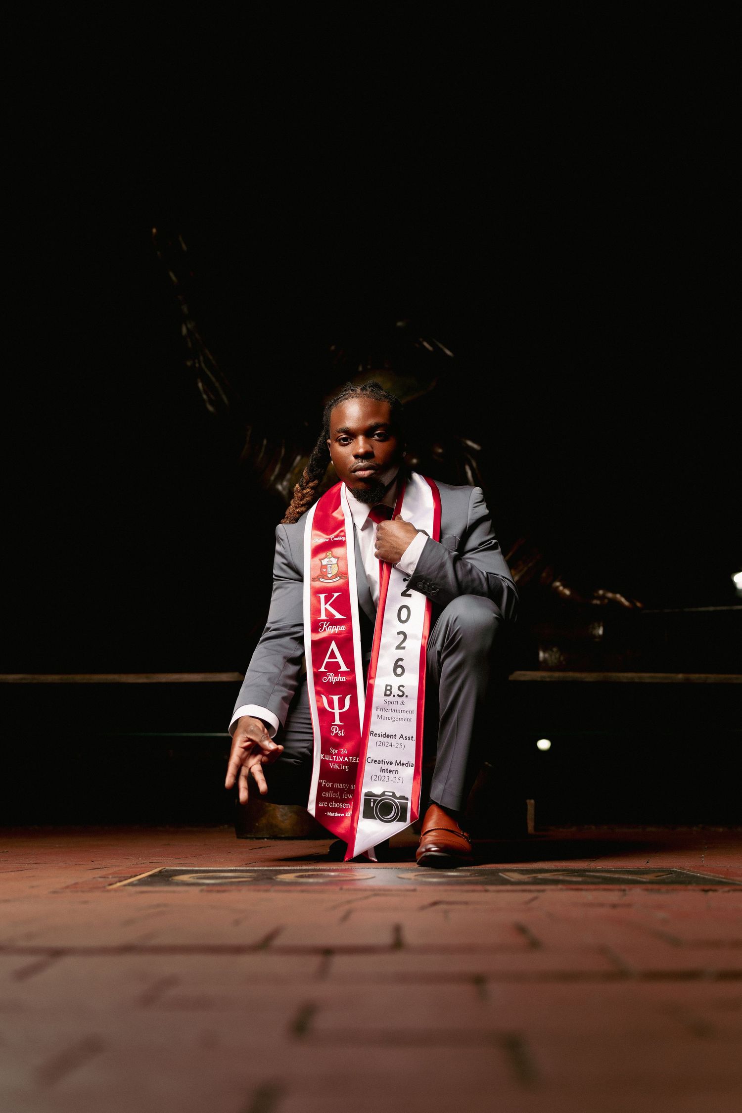 Young man in gray suit wearing Kappa Alpha Psi fraternity sash, posing confidently with 2026 graduation stole.