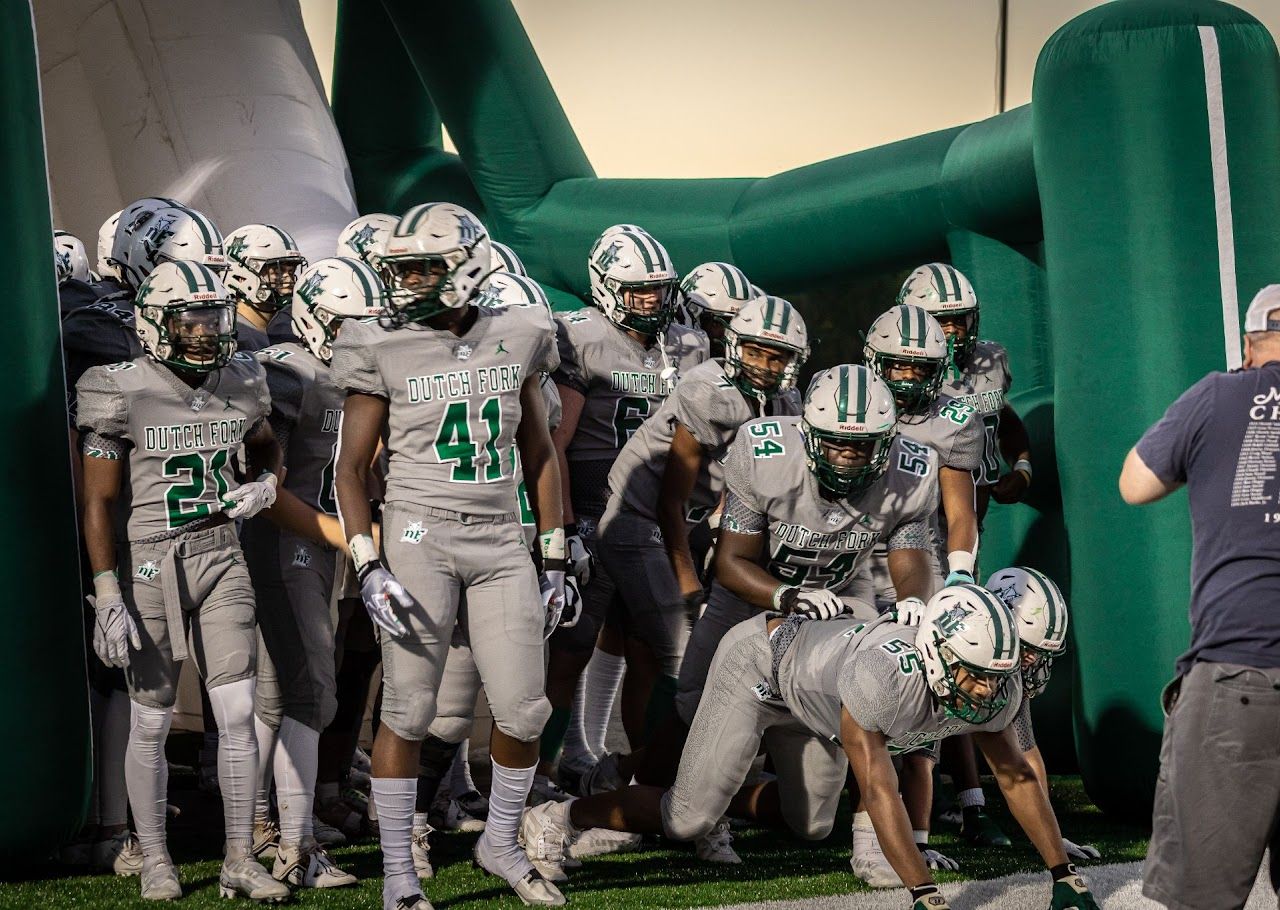 Football team in white uniforms and helmets prepares to exit a green tunnel before a game. DFHS