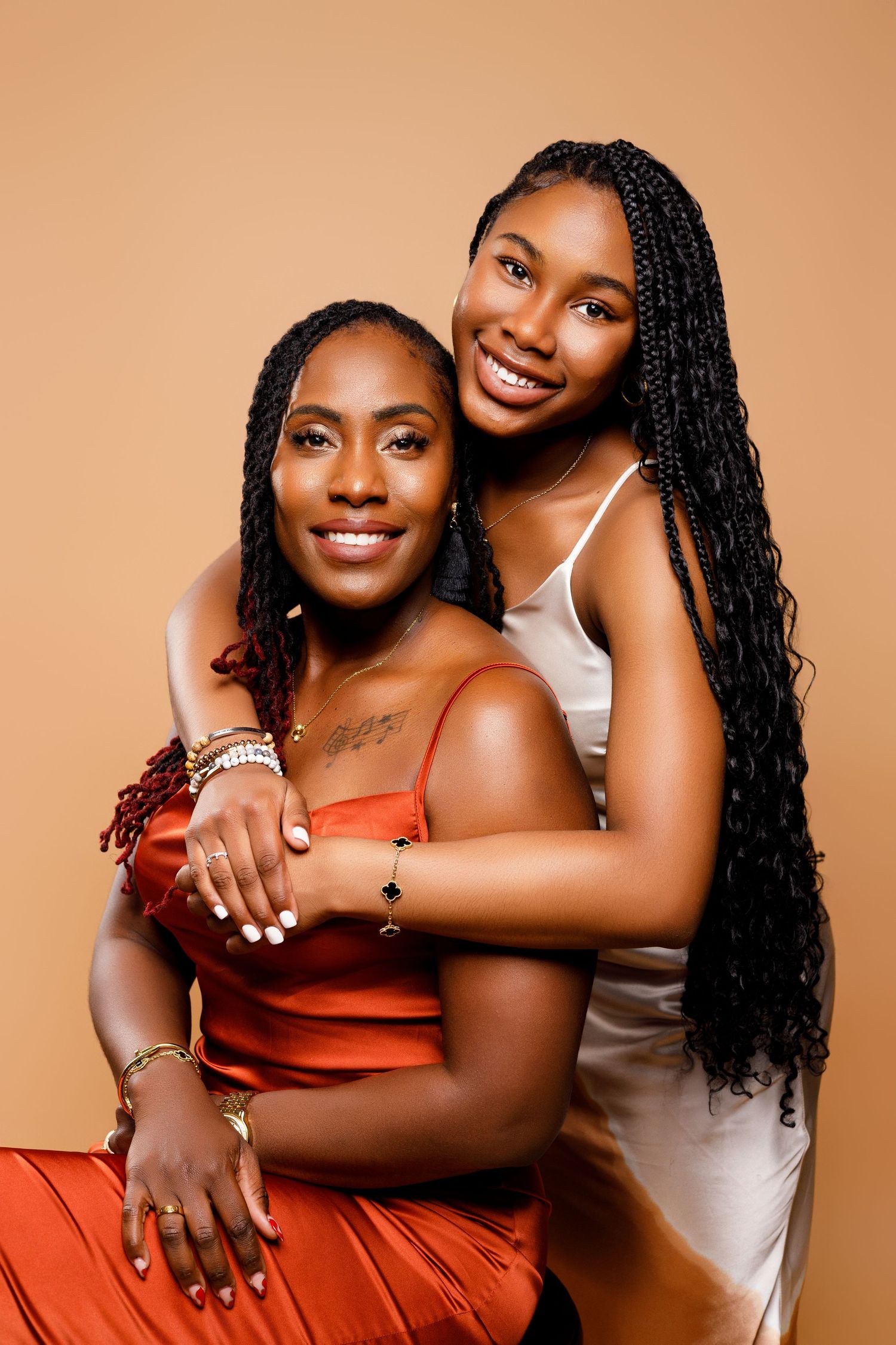 Two figures in contrasting outfits embrace warmly against peachy background.