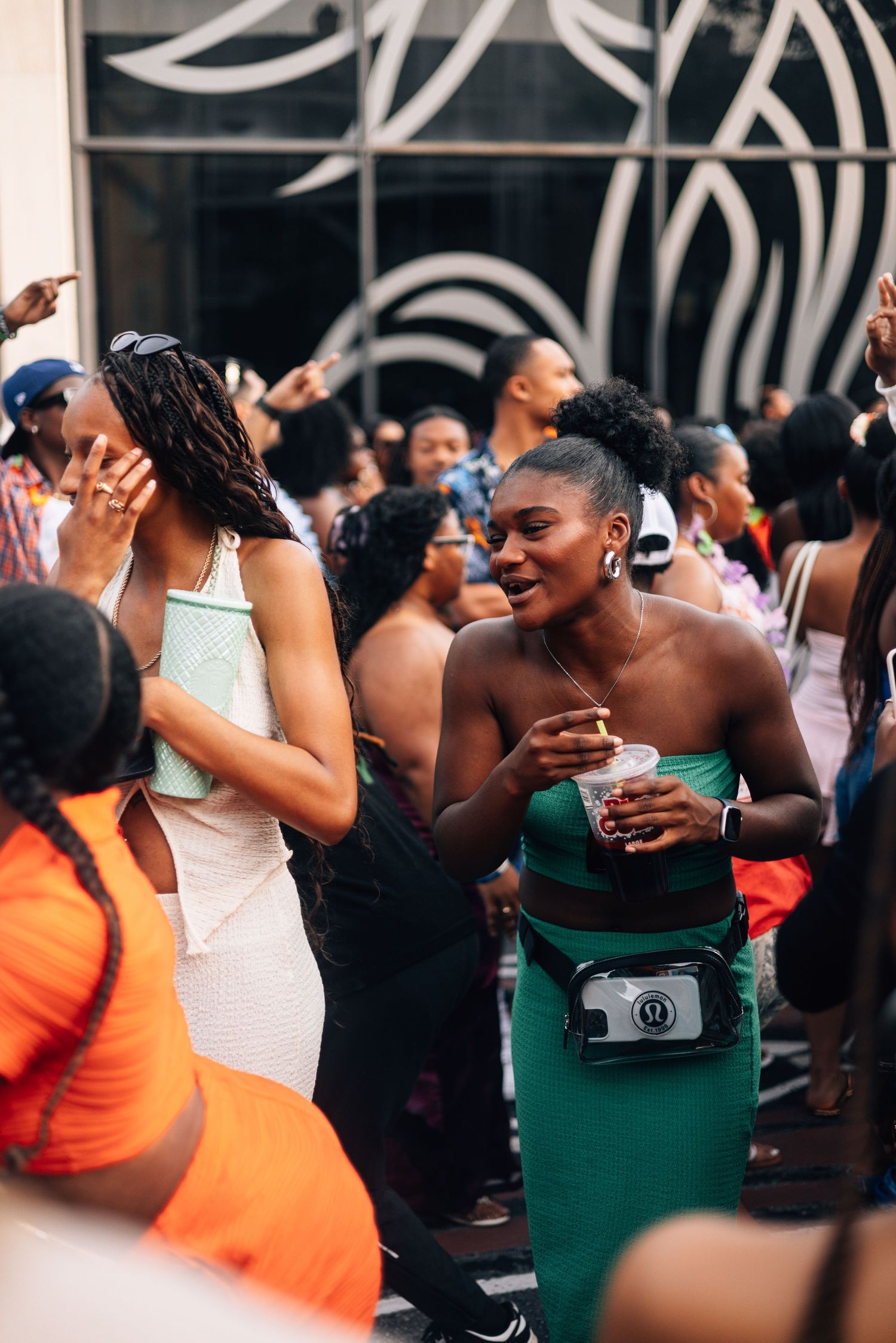 Crowd of people dancing and celebrating at a lively party with a woman in green dress and fanny pack in focus.