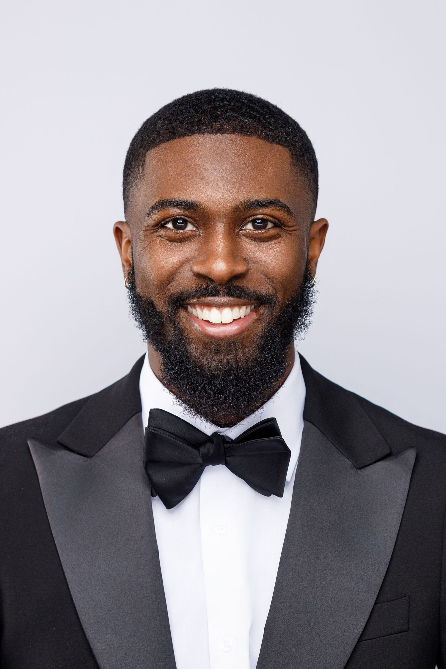 Professional portrait of someone wearing a black tuxedo with bow tie and displaying a bright, warm smile.