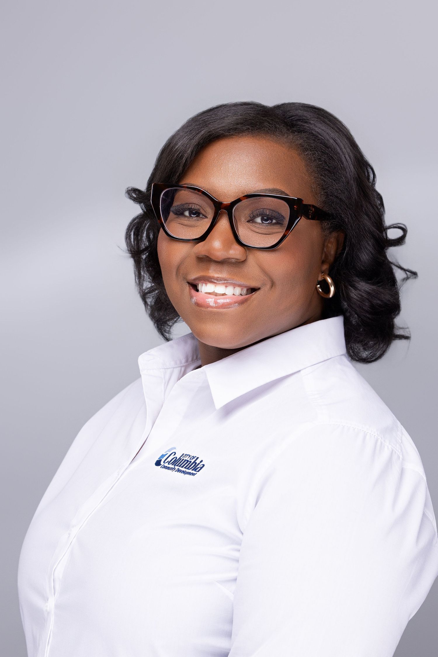 Professional headshots against a gray background showing a person in glasses and white collared shirt smiling warmly at the camera.
