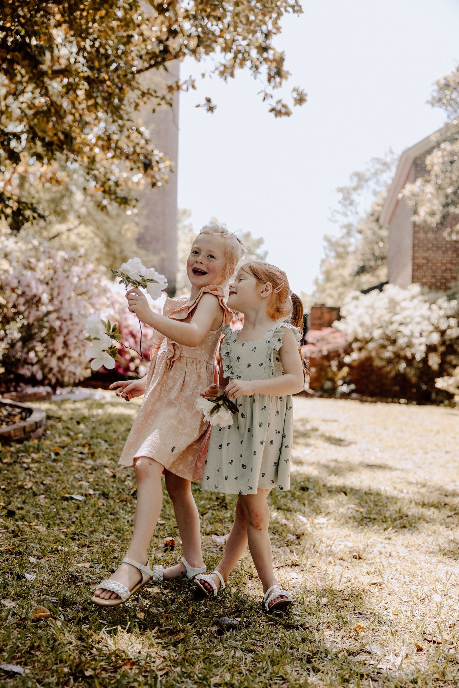 Two children in floral dresses playing and laughing in sunny garden.
