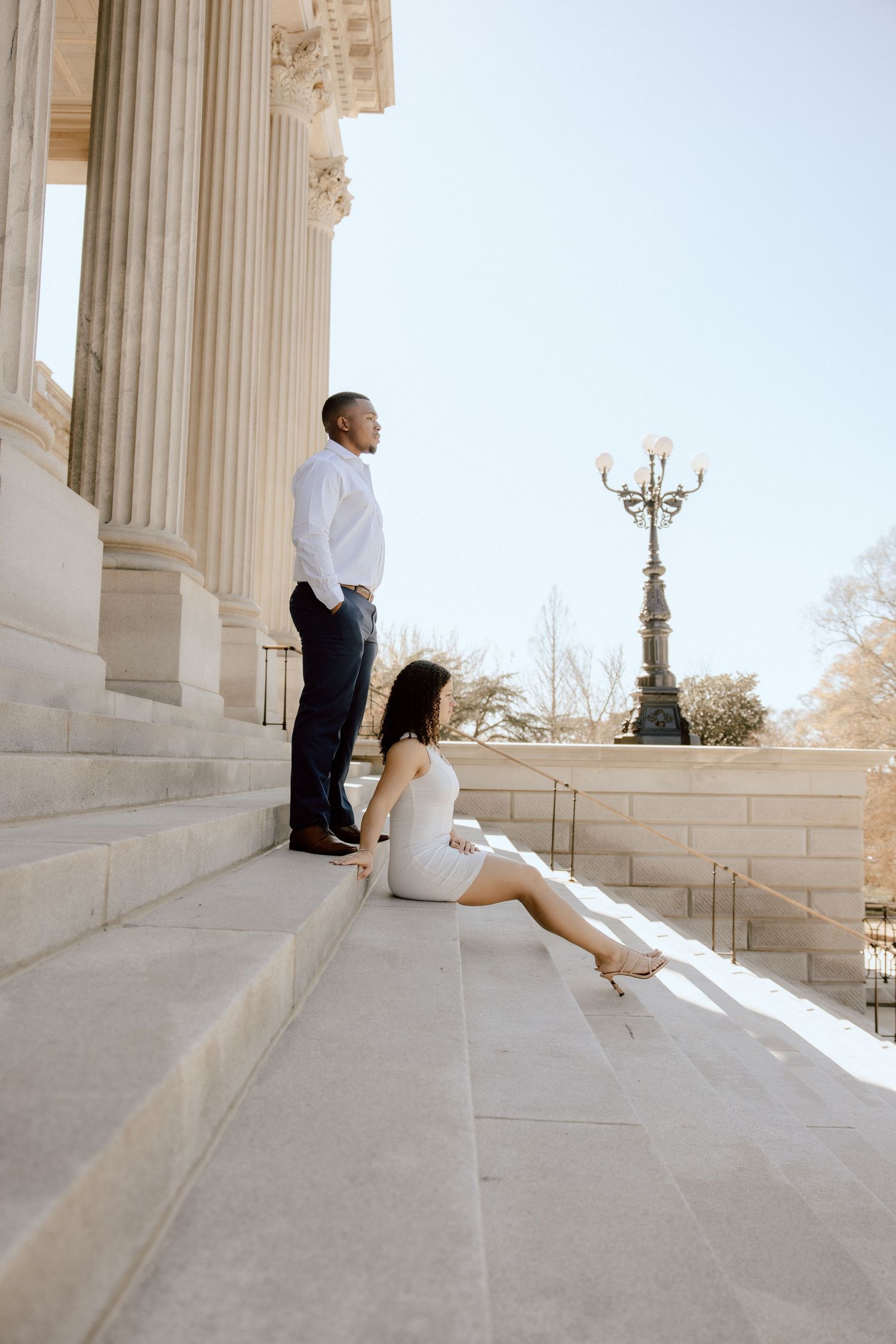 Couple relaxes on grand stone steps beside classical architecture.