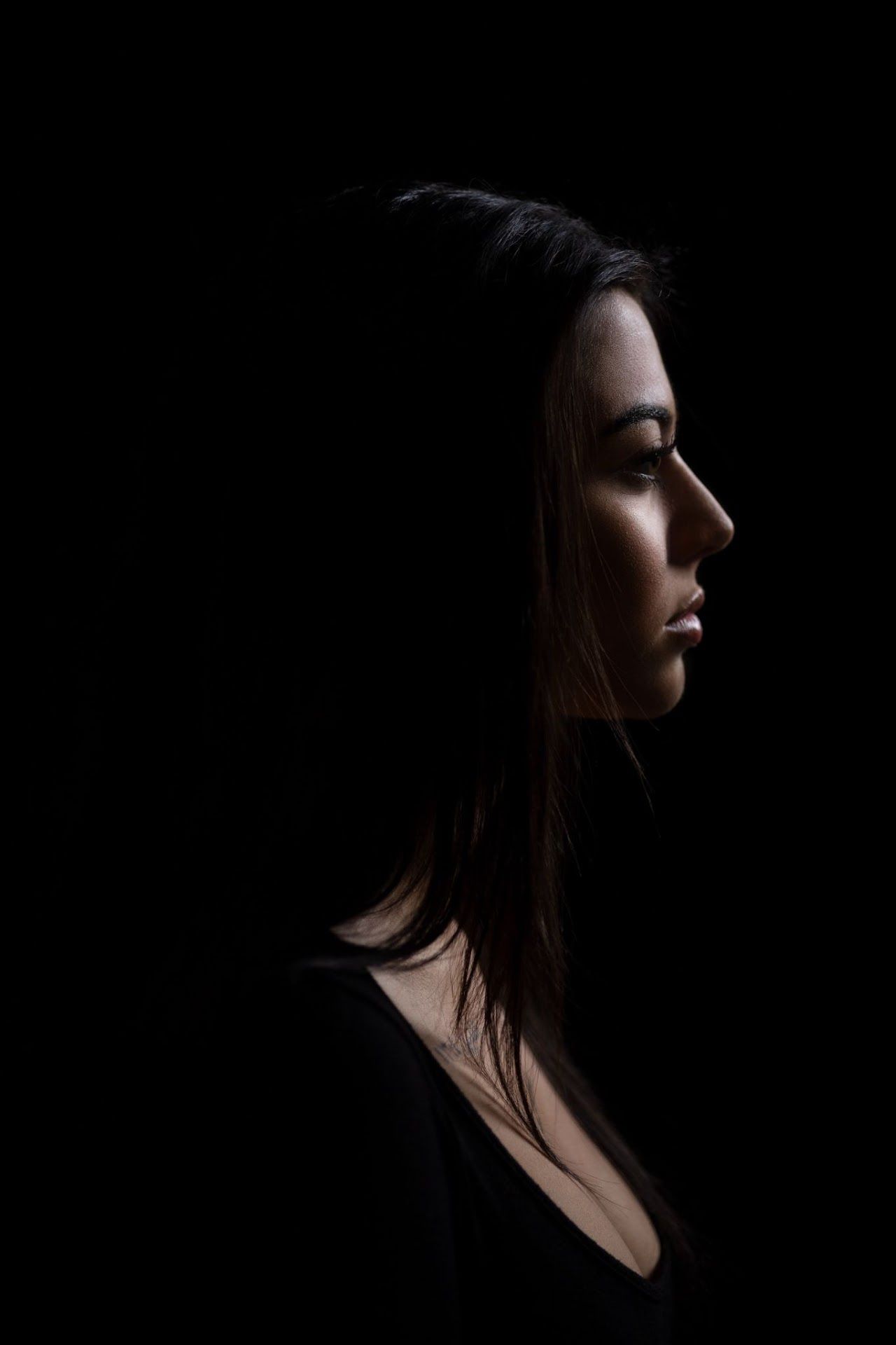 Dramatic side profile silhouette portrait against black background with minimal lighting highlighting facial features.