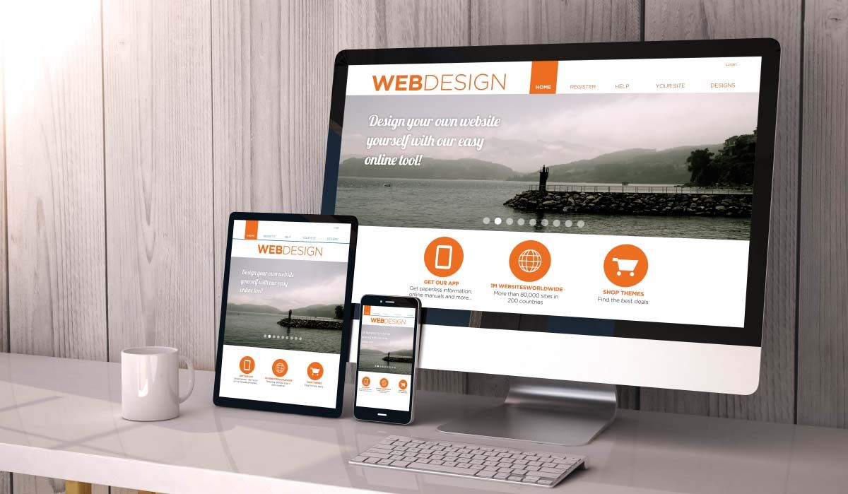 Responsive website design mockup displayed across desktop computer, tablet, and smartphone on white desk.