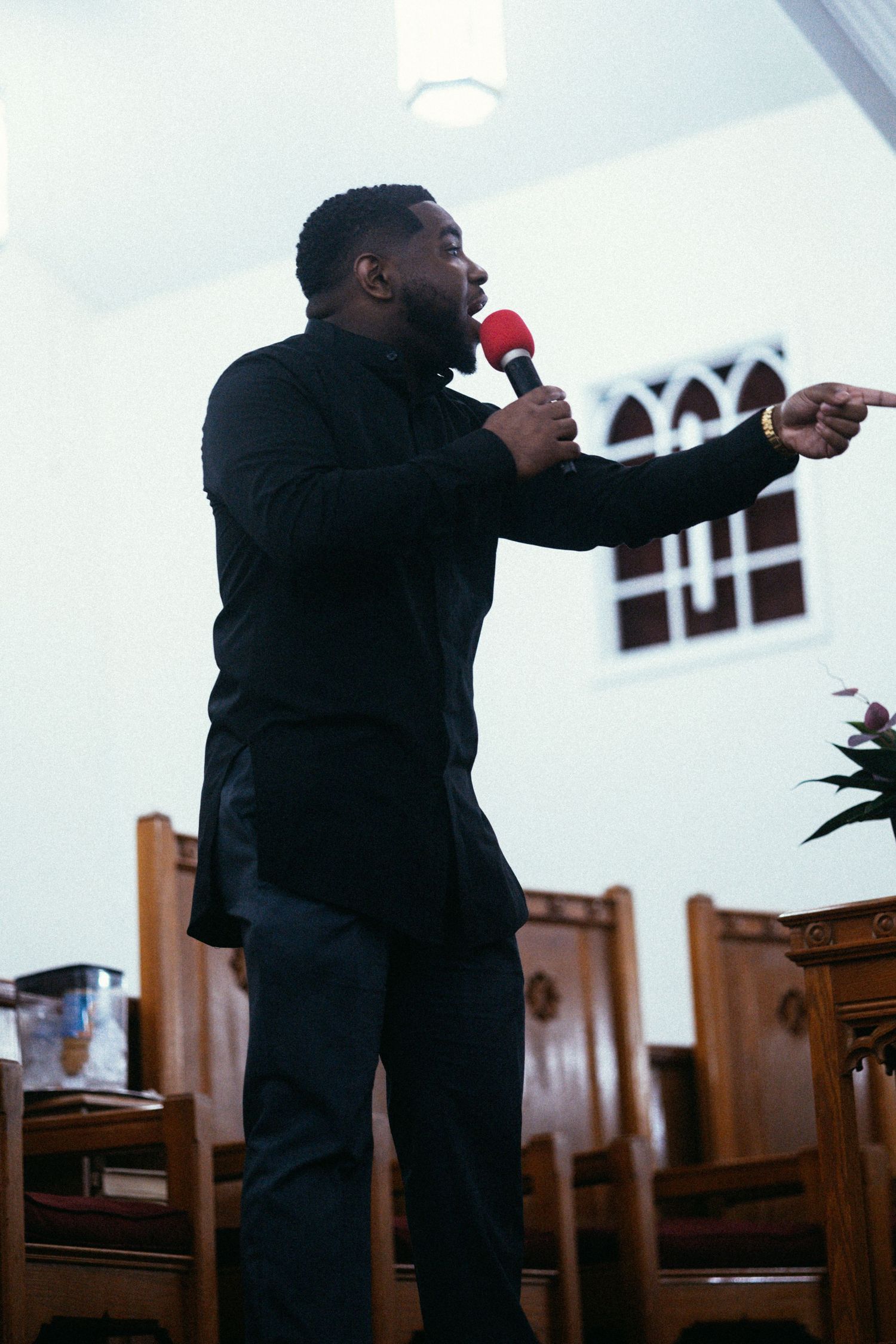 A passionate speaker delivers a message at a church podium with arched windows in the background.