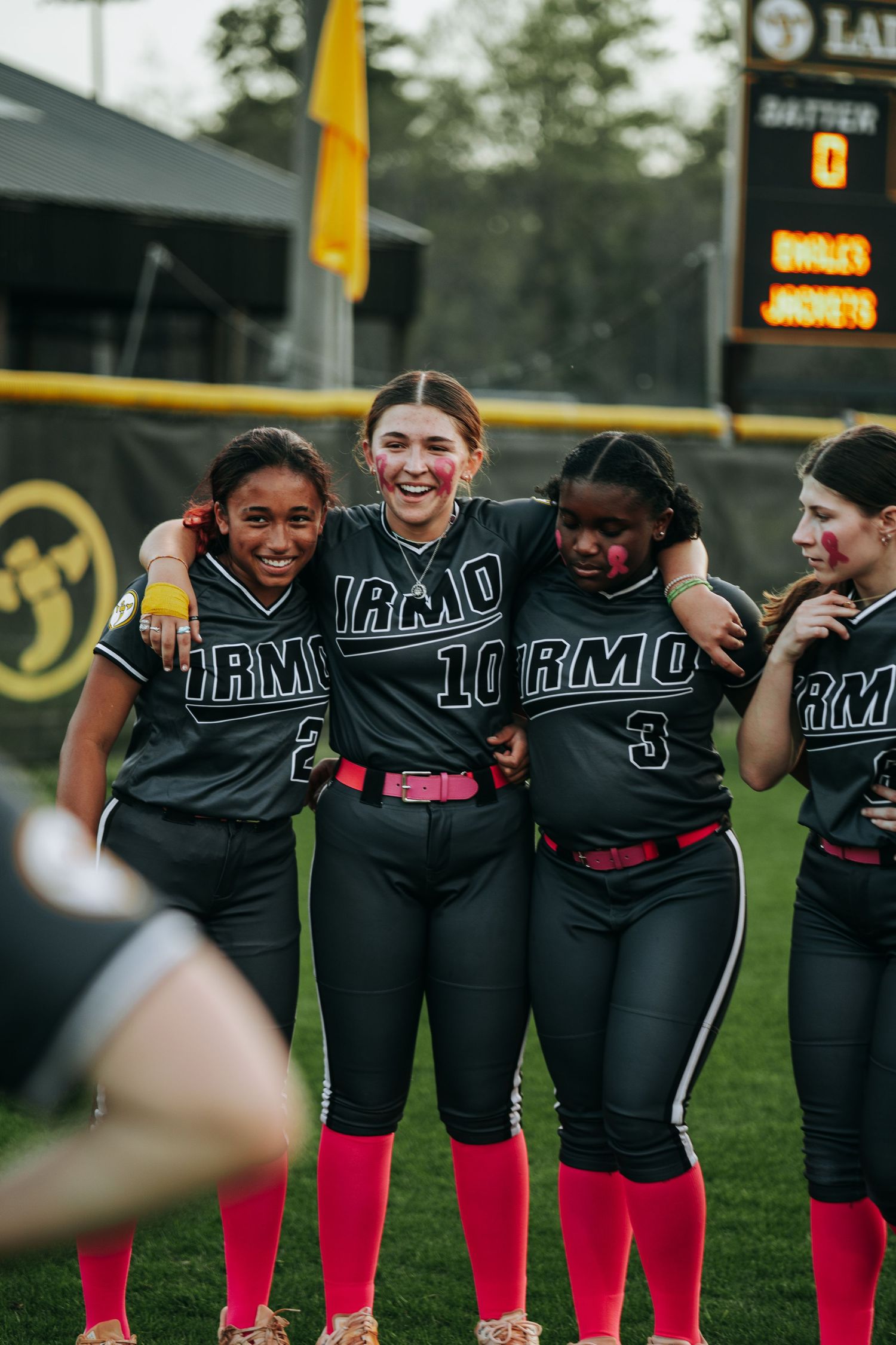 Irmo HS Softball team in black uniforms with pink accents posing together on field.