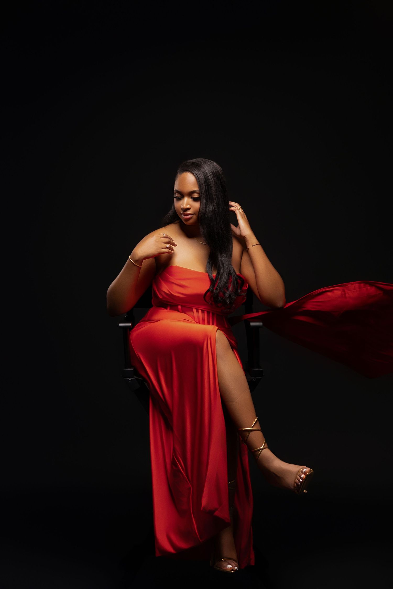 Elegant flowing red dress catches movement in dramatic dark studio portrait.