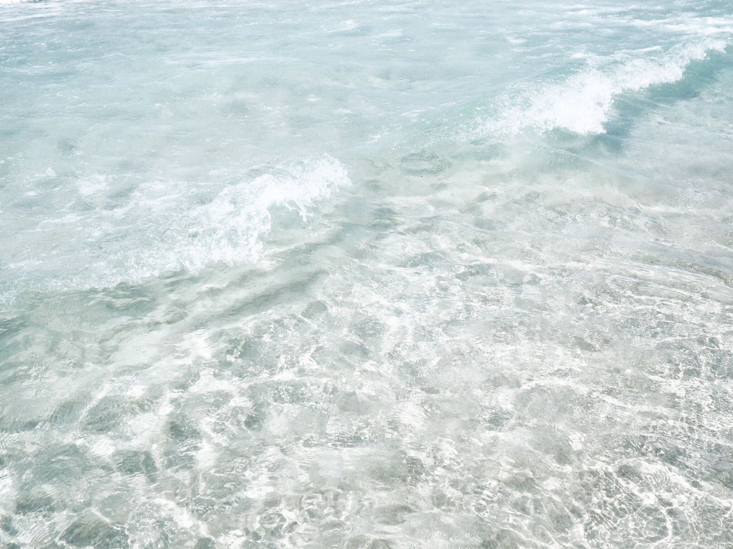 Close-up aerial view of ocean waves crashing and rolling along the shoreline with white foam and turquoise water.
