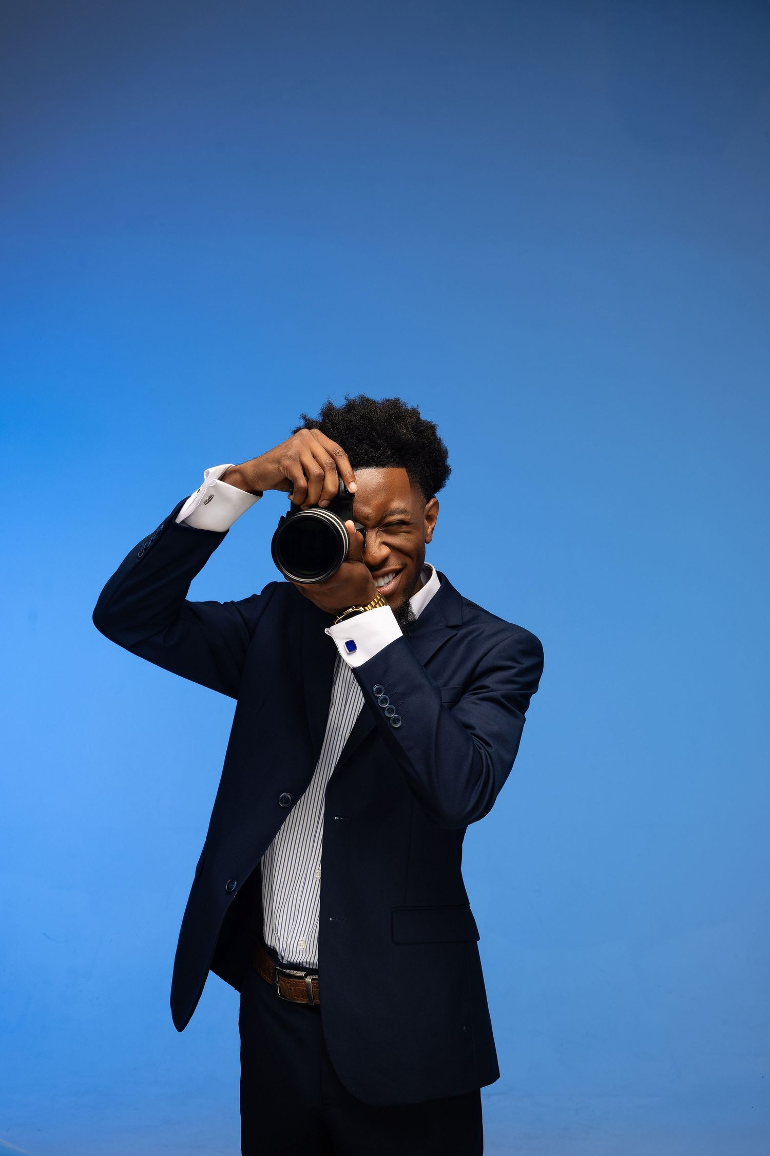 Professional photographer in navy suit taking photo with DSLR camera against blue background.
